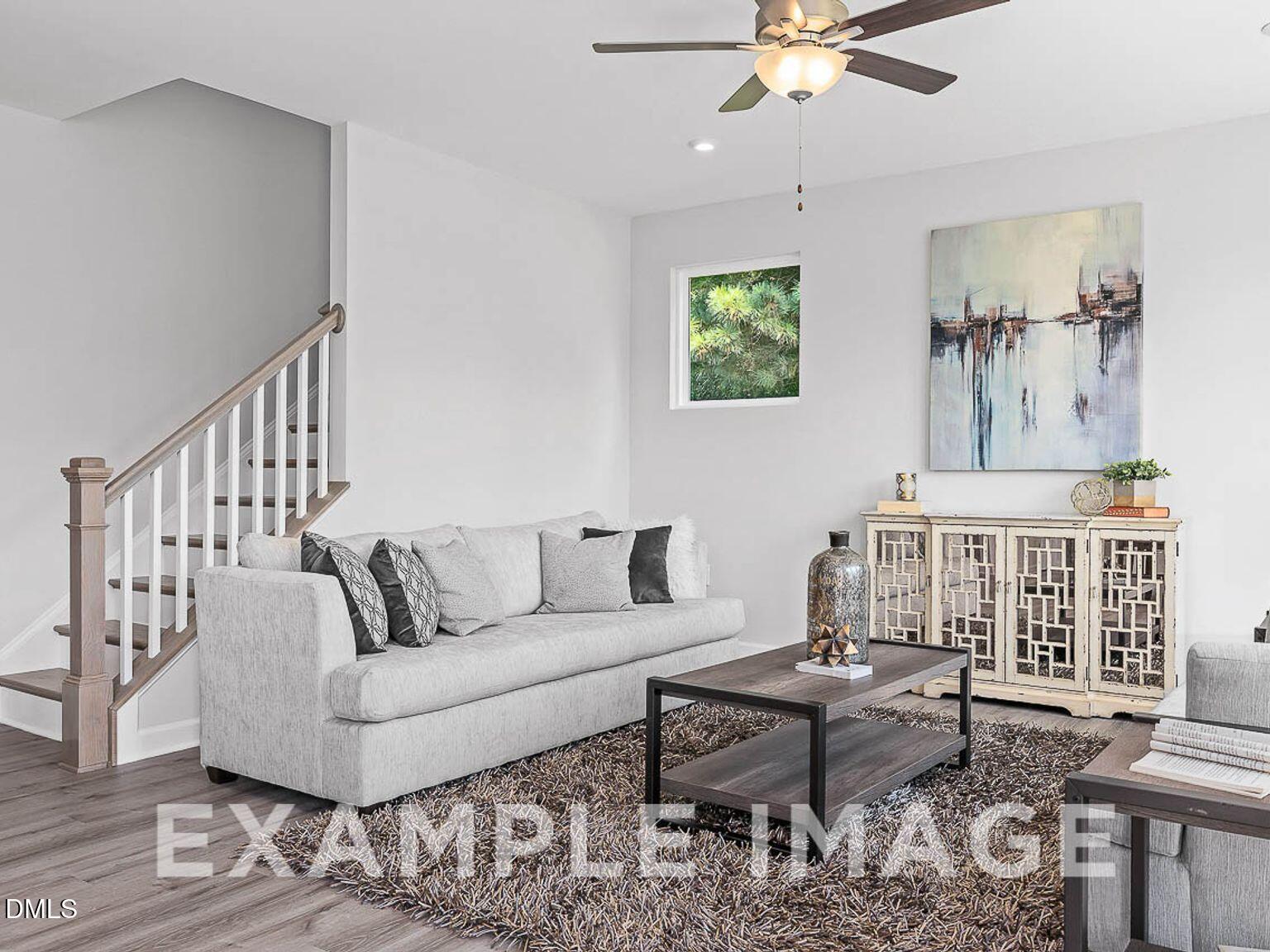 Cozy living room with gray sofa, wooden coffee table, area rug, ceiling fan, and staircase in Davidson Homes The Chestnut B, Lillington, NC