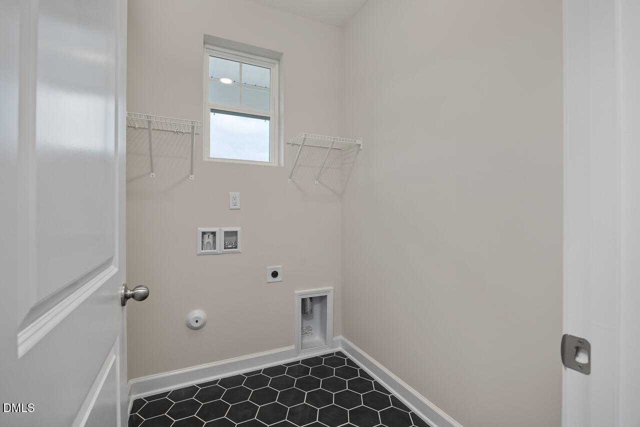 Functional laundry room with white utility sink, washer/dryer hookups, hanging rods, window, and black hex tile floor in Davidson Homes The Carter C, Lillington, NC