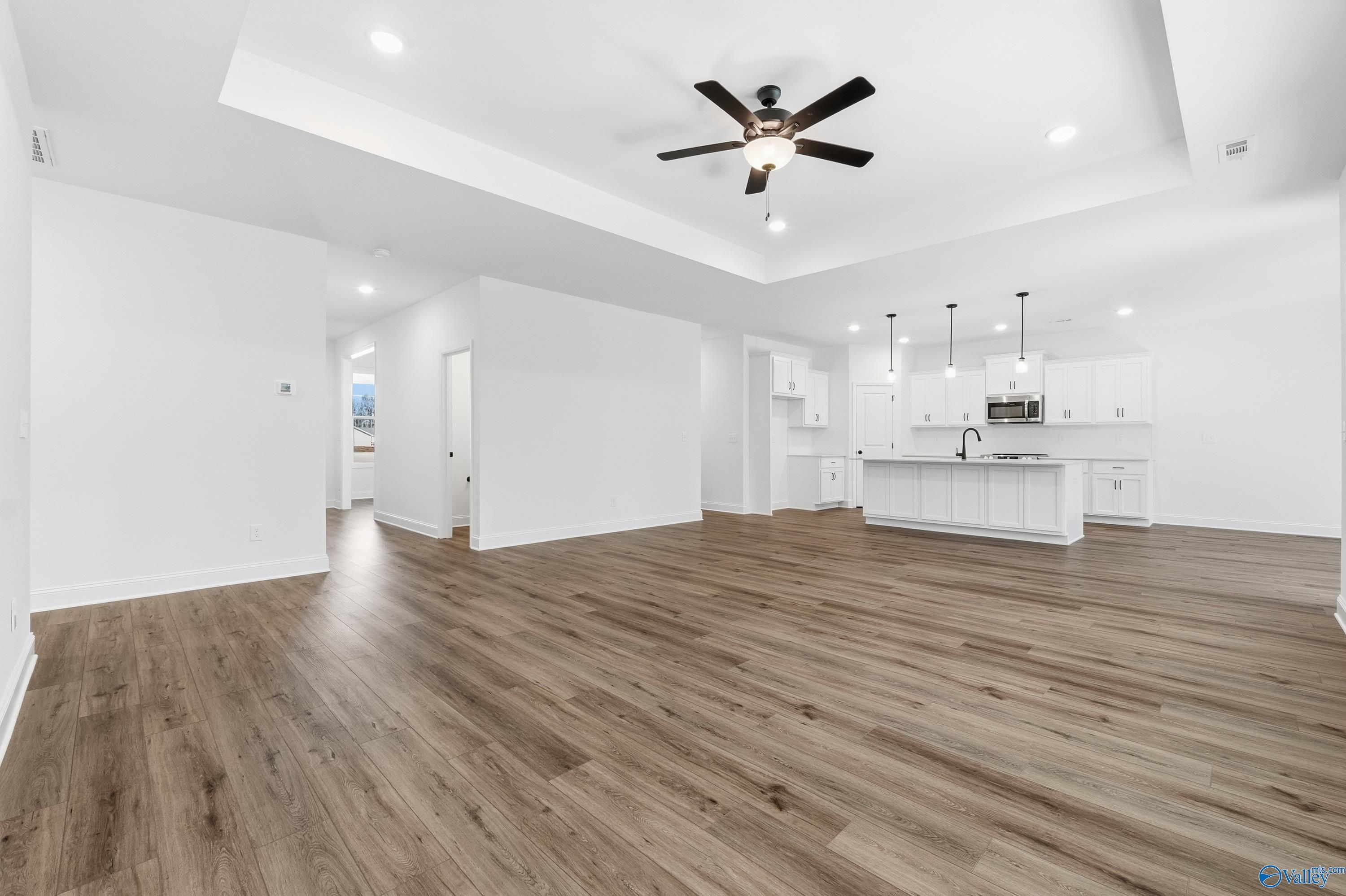 Open-concept kitchen and living area with white island, hardwood floors, ceiling fan in Davidson Homes The Rockford D, Hazel Green, Alabama