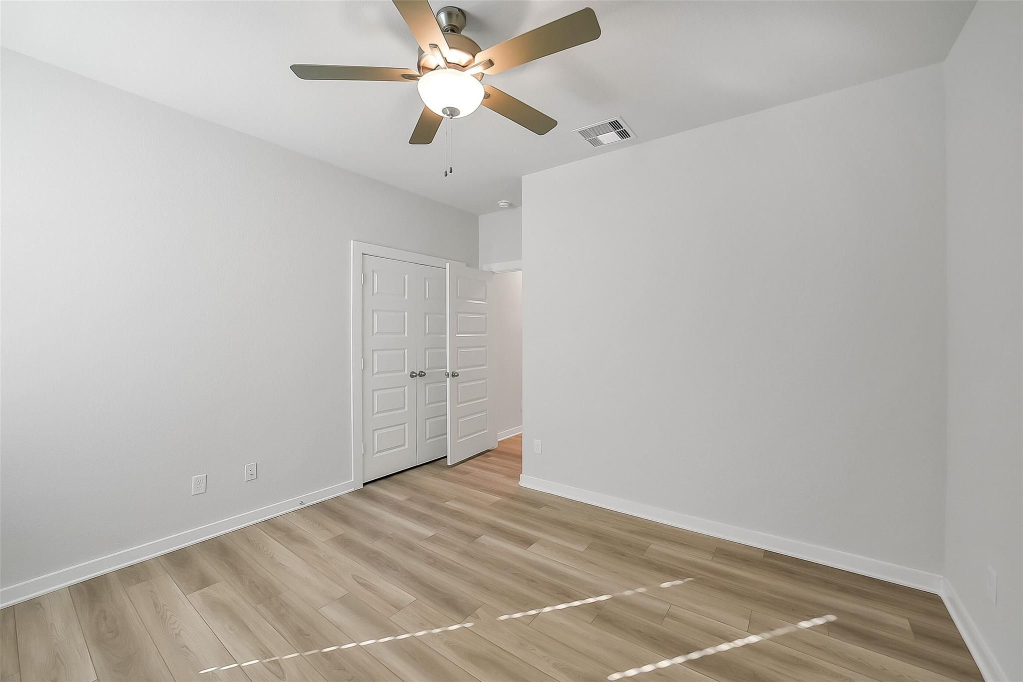 Bright empty bedroom with ceiling fan, light wood floors, and double doors in Davidson Homes The Acadia A, Sunterra, Katy, Texas