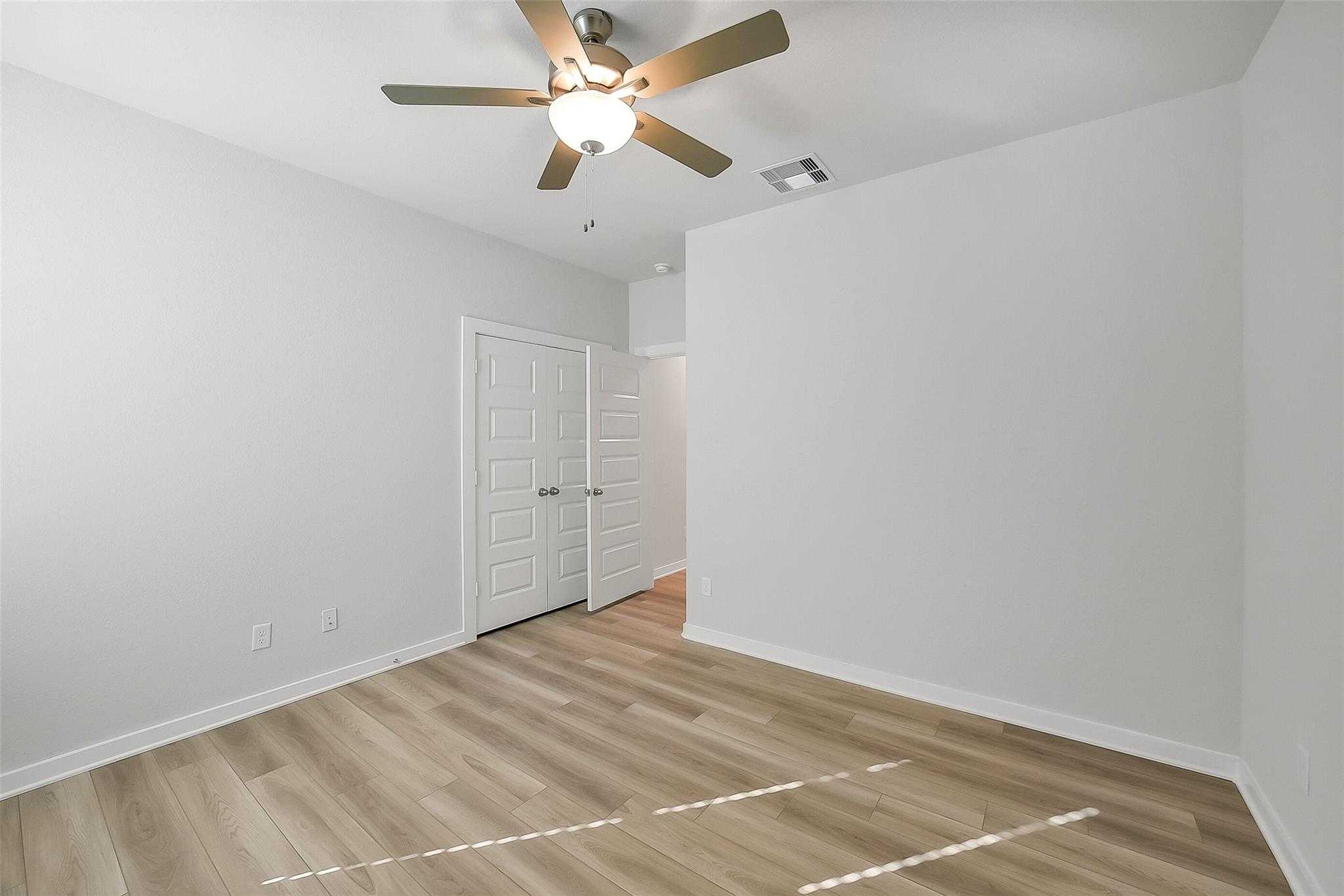 Bright empty bedroom with ceiling fan, light wood floors, and double doors in Davidson Homes The Acadia A, Sunterra, Katy, Texas