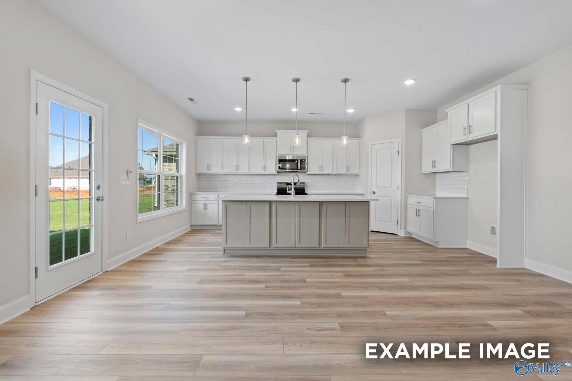 Bright open-concept kitchen with white shaker cabinets, gray island, stainless appliances, and backyard view in Davidson Homes Madison A, Toney, AL