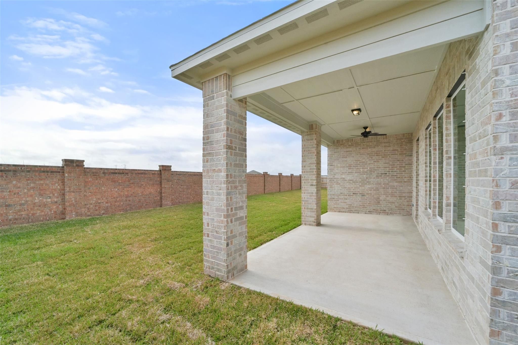 Covered patio with ceiling fan and brick columns overlooking lush green yard in Davidson Homes The Zion A, Lago Mar, Texas City, Texas