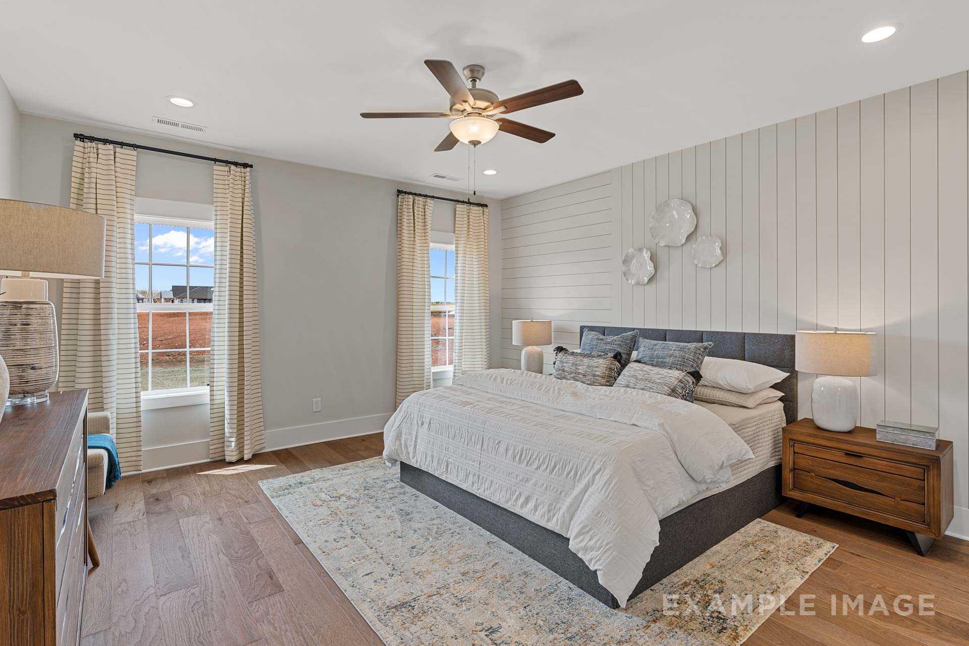Spacious master bedroom in The Rockford featuring king bed, shiplap wall, ceiling fan, large window, hardwood floors