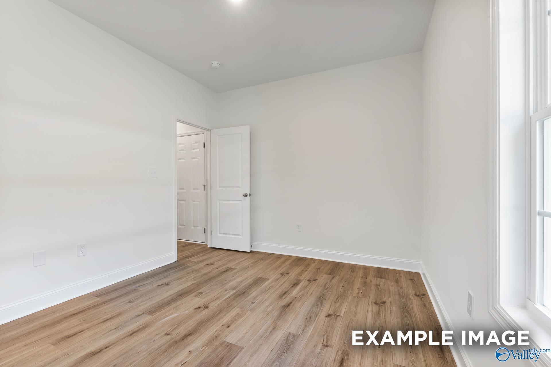 Bright bedroom with light hardwood floors, white walls, and large window in 4-bedroom The Daphne V home by Davidson Homes, Athens, Alabama