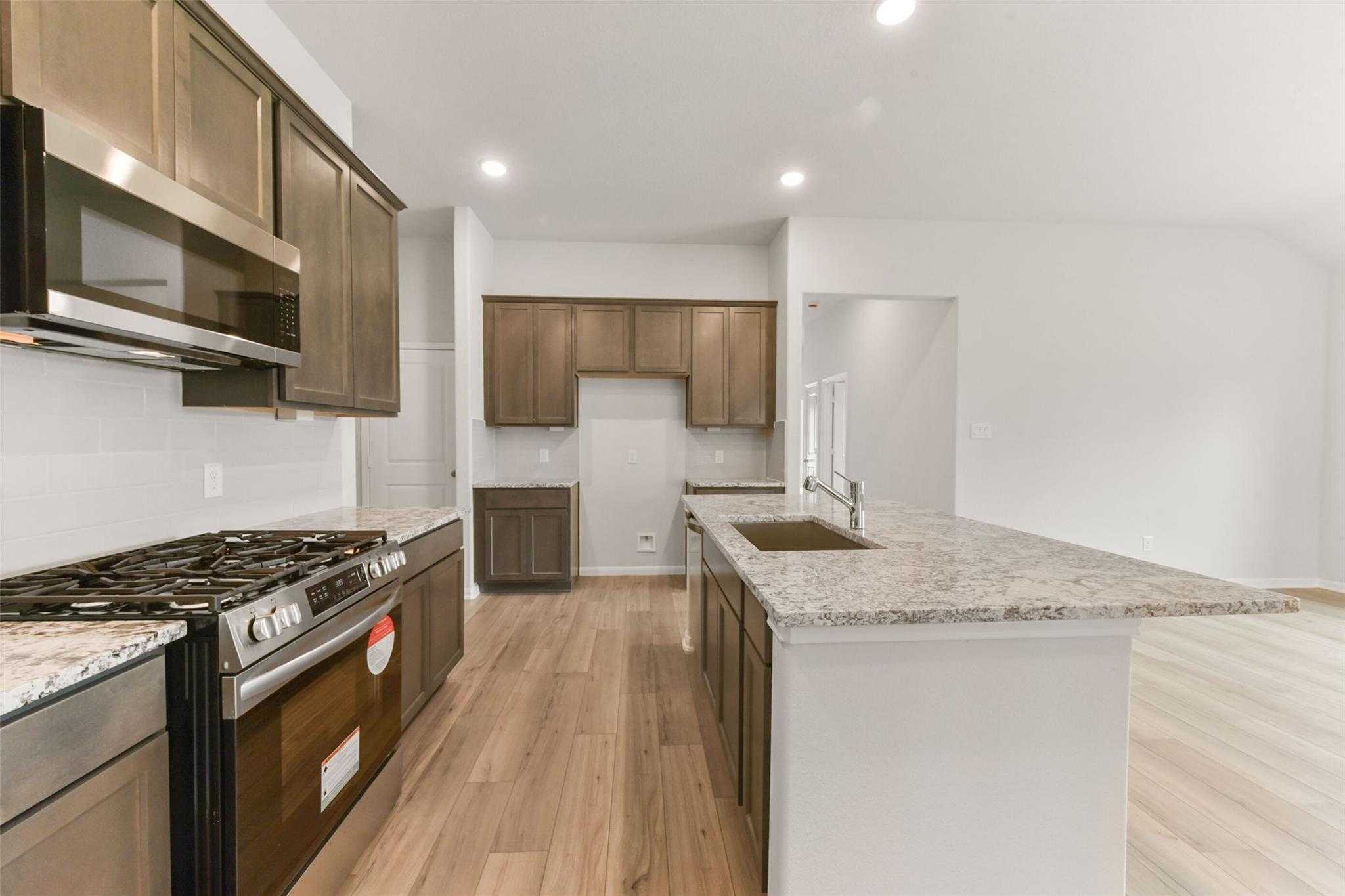 Modern kitchen with shaker cabinets, granite island sink, stainless steel appliances in The Laguna B, Magnolia, Texas