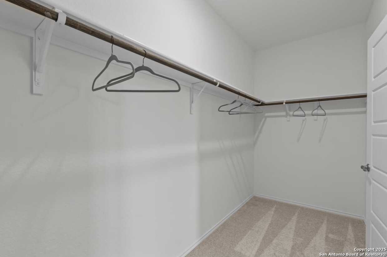 Spacious walk-in closet with wooden rods, white walls, and carpet floor in Davidson Homes The Daphne J, Elmendorf, Texas
