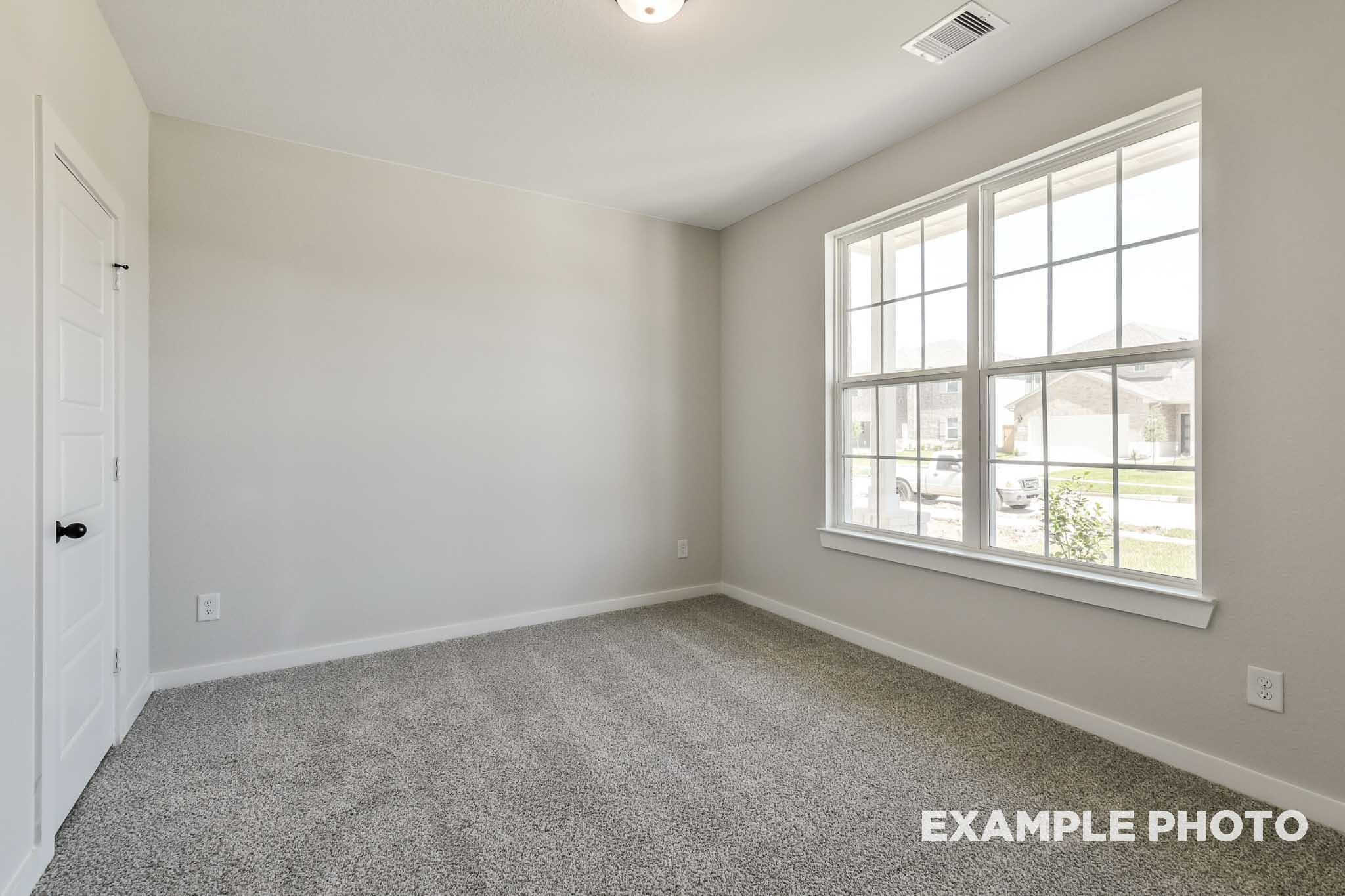 Spacious secondary bedroom in The Daphne G with large window, beige carpet, light gray walls, and neutral tones