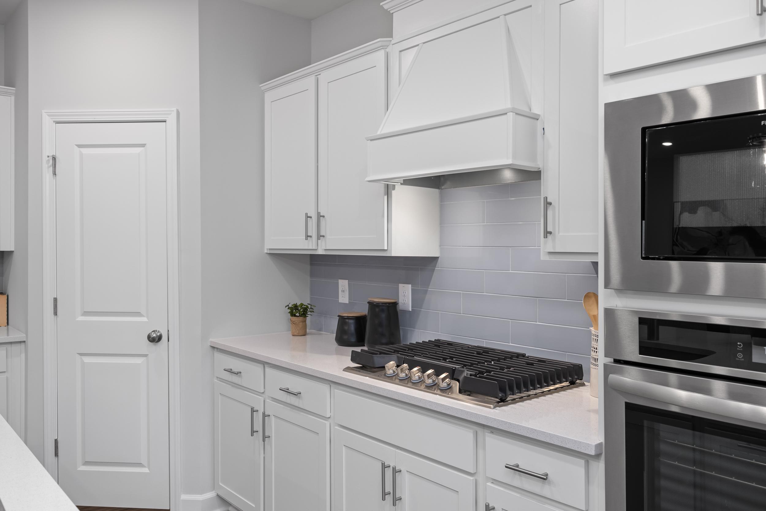 Modern kitchen in The Warren featuring white shaker cabinets, a gas cooktop, and a sleek tile backsplash.