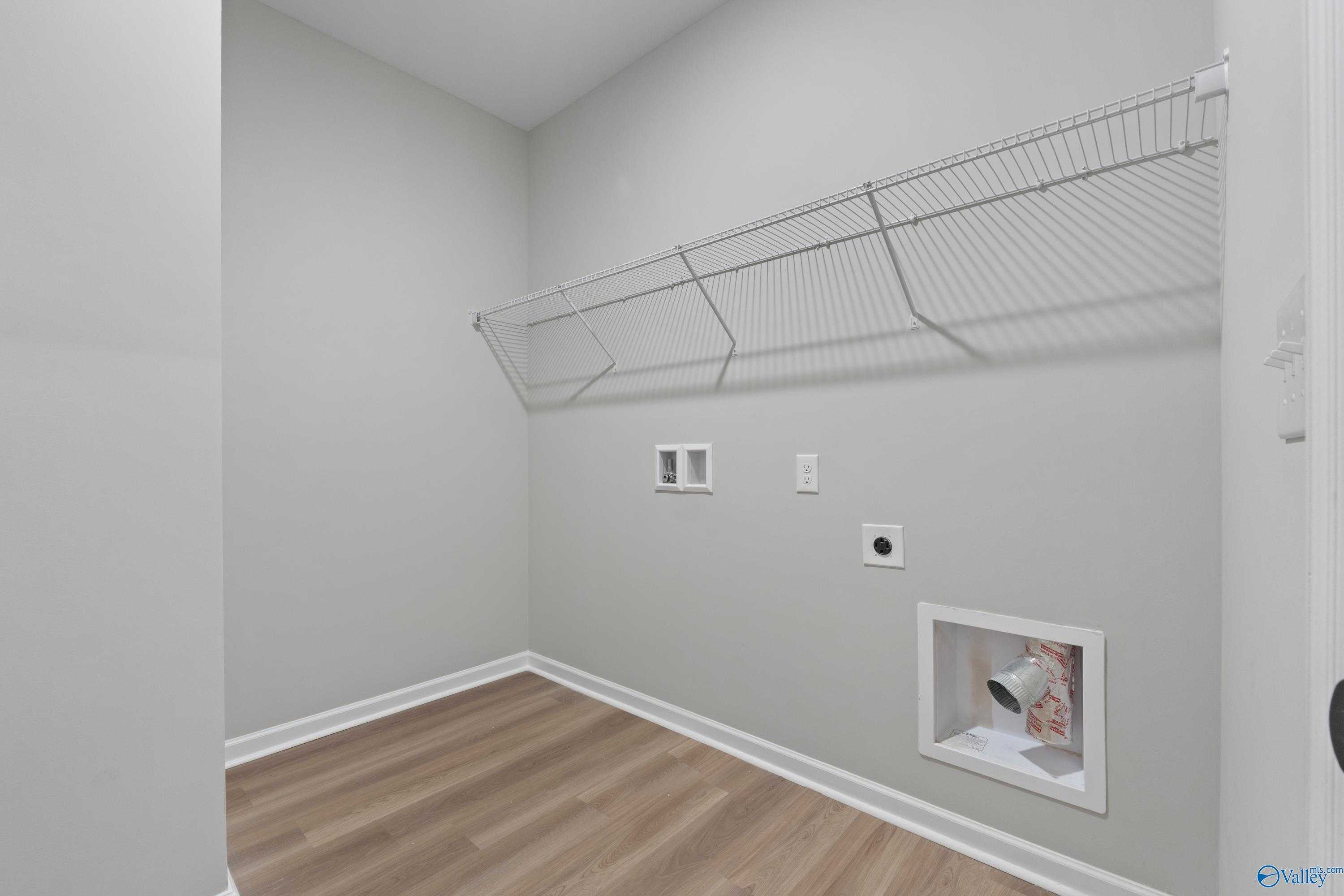 Modern laundry room with wire shelving, washer-dryer outlets, utility vent, and laminate flooring in Davidson Homes The Phoenix, Fayetteville TN