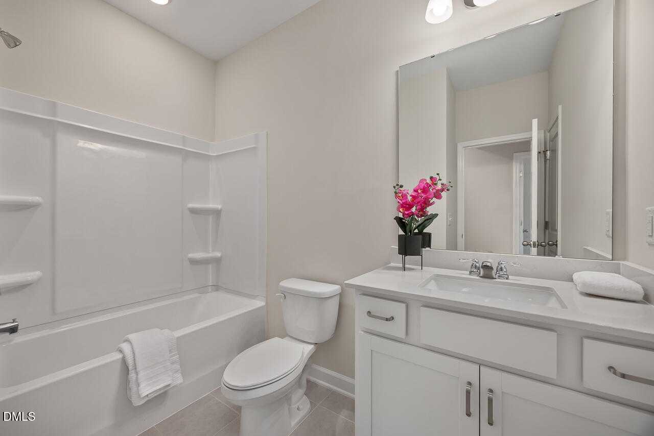 Bright secondary bathroom with white tub, glass shower, single vanity, large mirror in Davidson Homes The Carter C, Lillington, NC