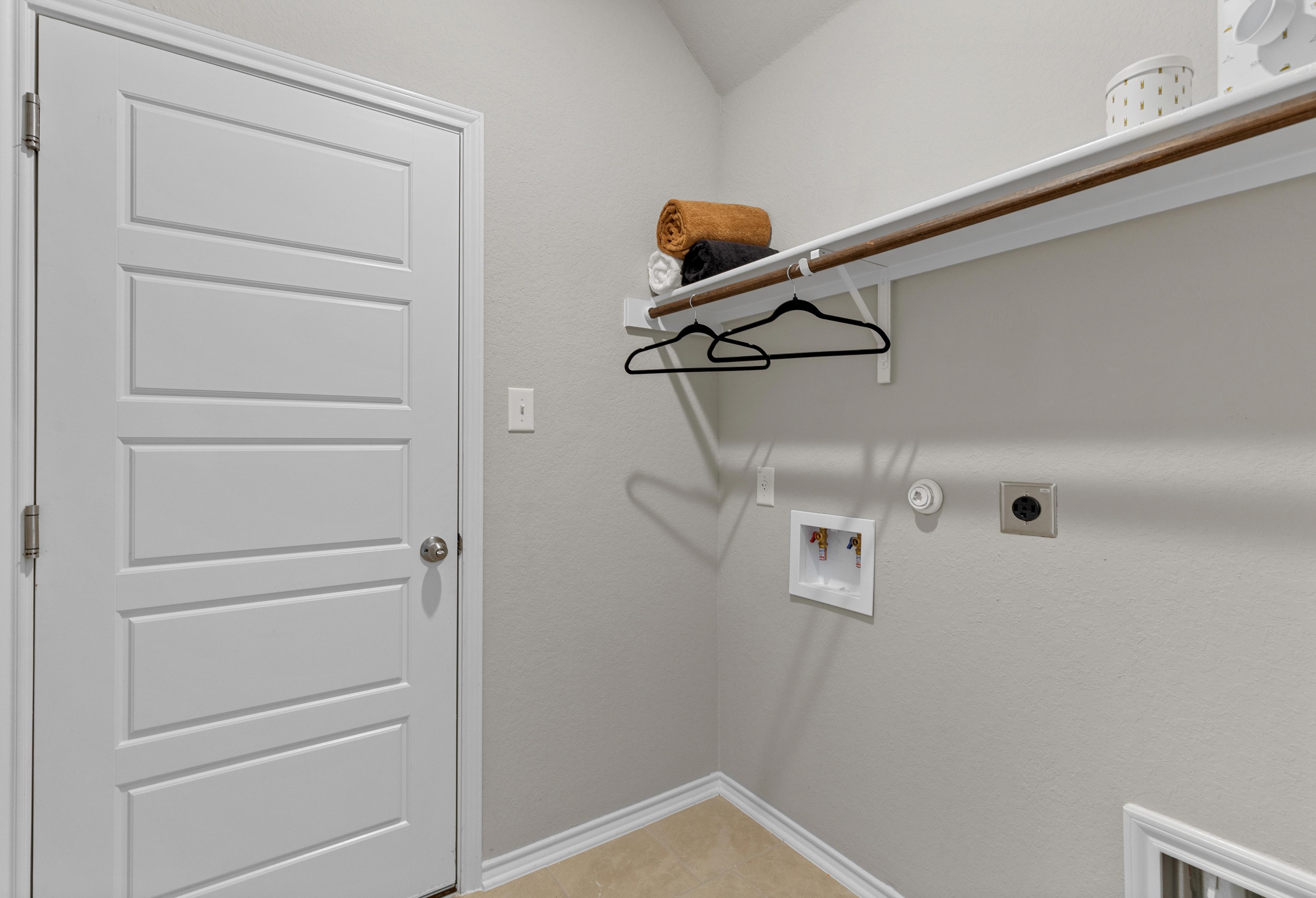 The Sabine A laundry room featuring beige walls, white paneled door, built-in shelf with orange towel, and washer dryer hookups
