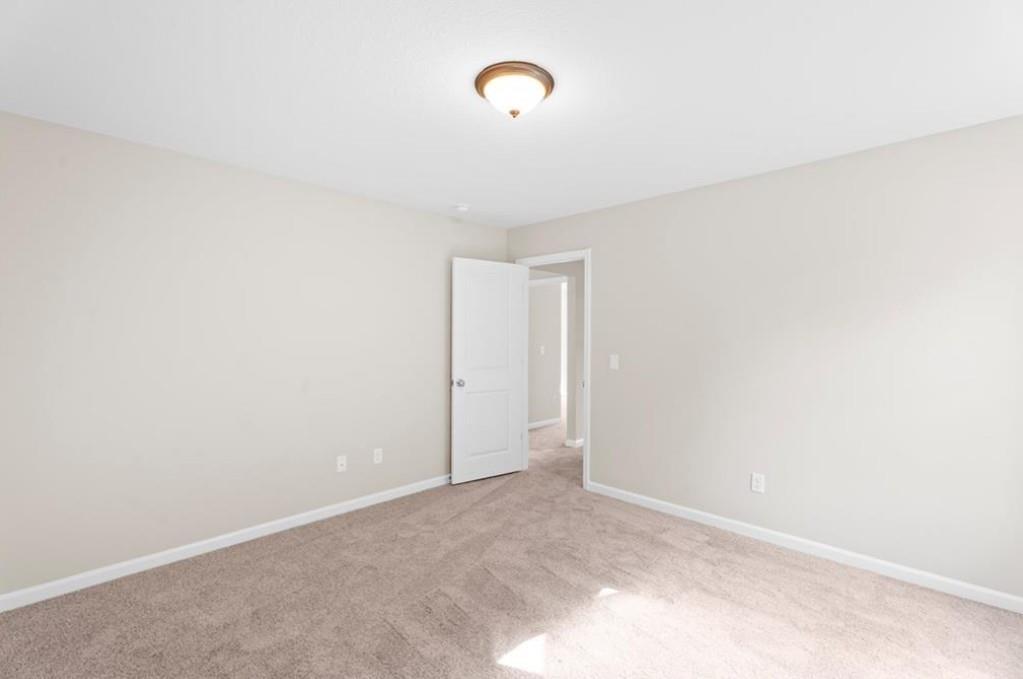 Spacious empty bedroom with beige walls, tan carpet, open door to hallway in Davidson Homes The Washington, Phenix City, Alabama