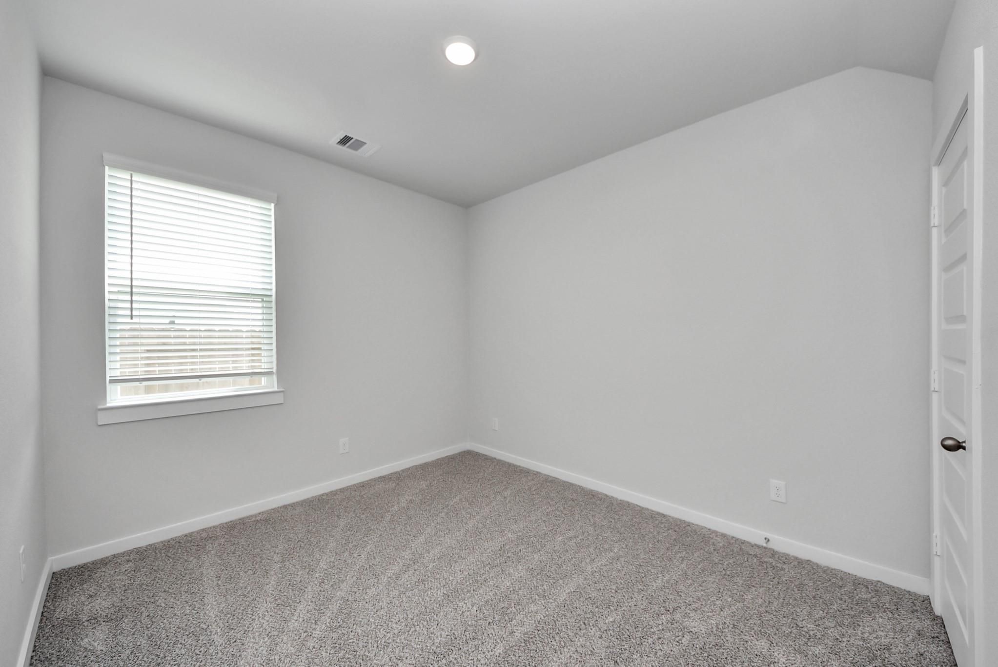 Bright empty bedroom with carpet, white walls, and window blinds in Davidson Homes The San Marcos E, Beasley, Texas