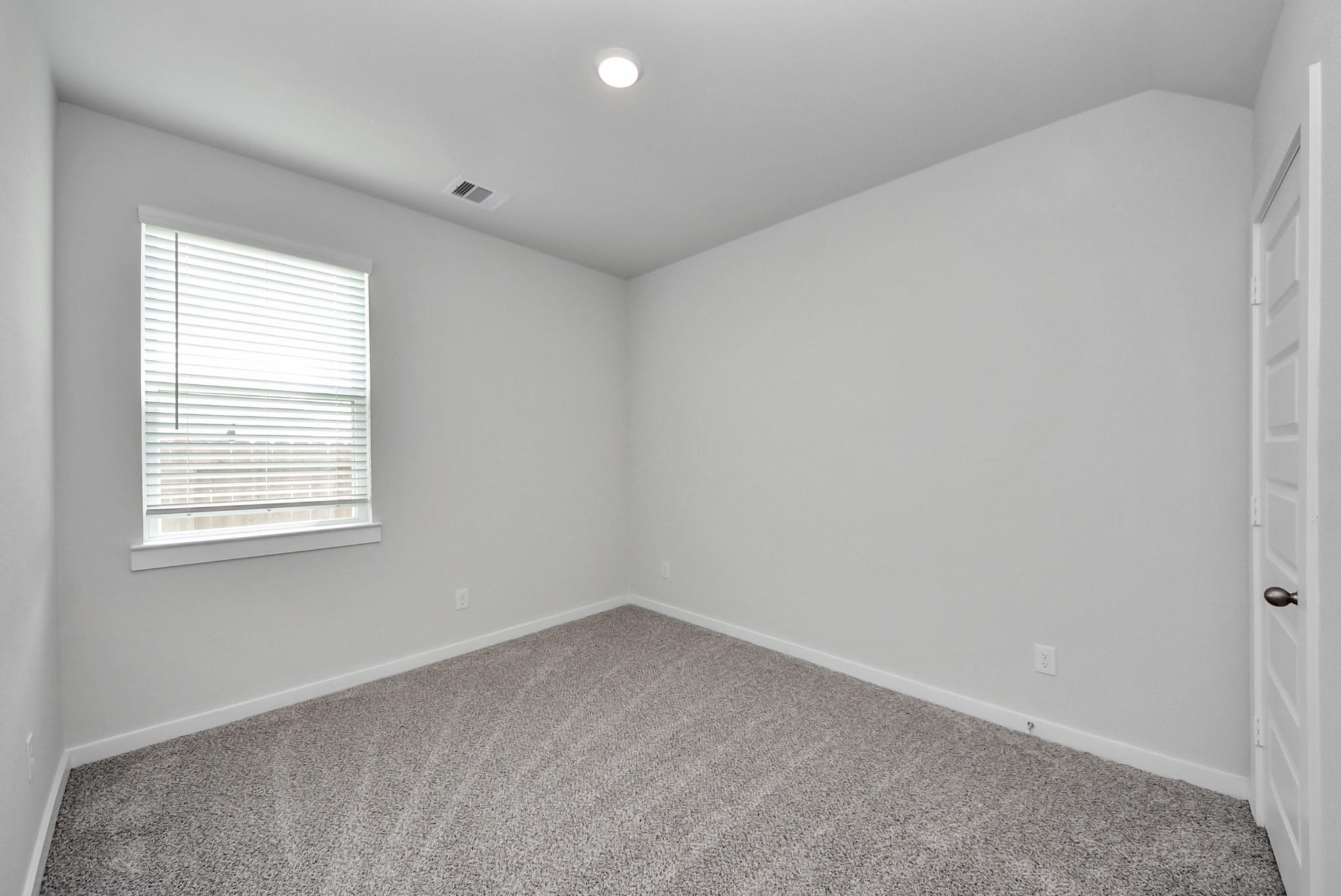 Bright empty bedroom with carpet, white walls, and window blinds in Davidson Homes The San Marcos E, Beasley, Texas