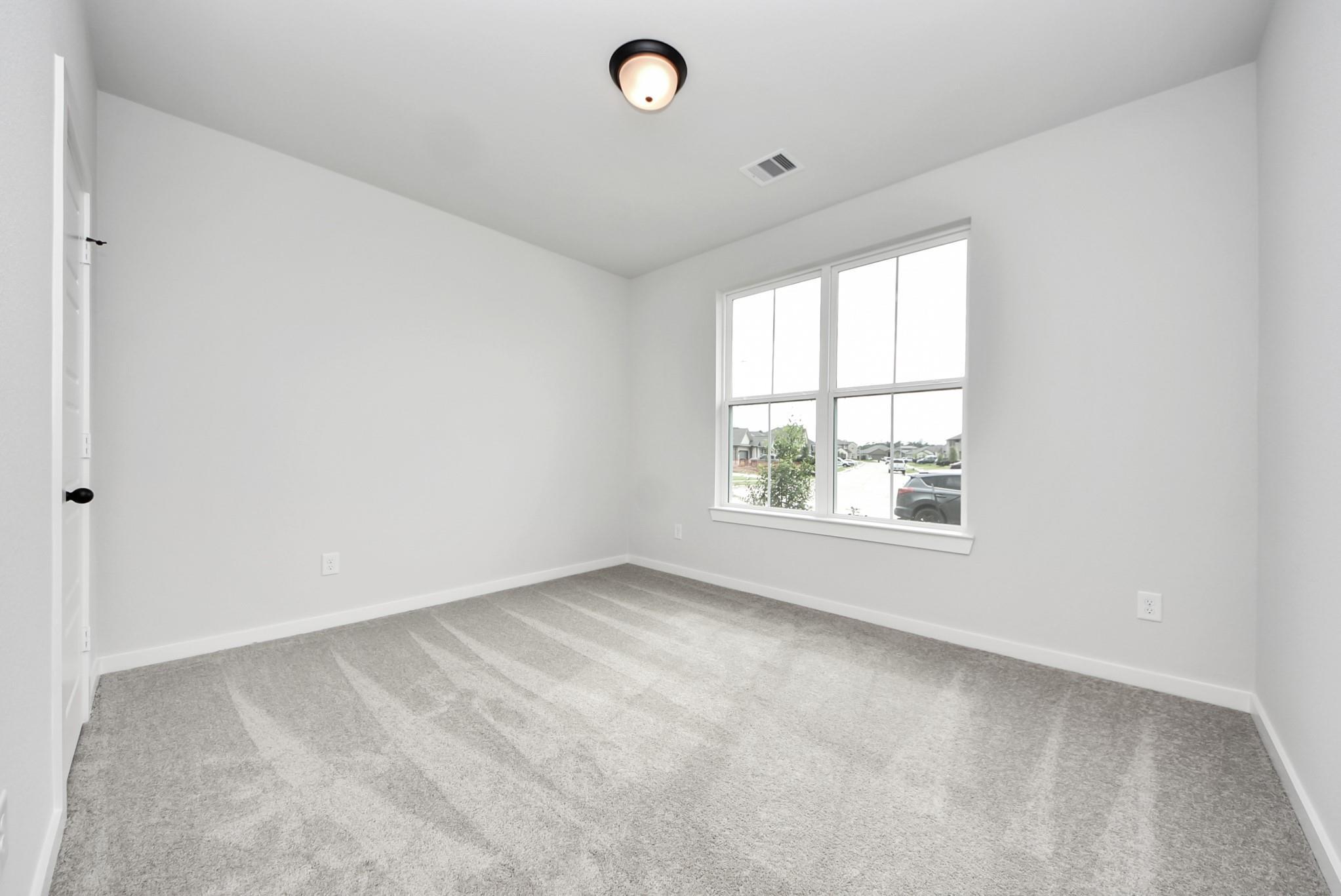 Bright, carpeted bedroom with large window in The Daphne F floor plan at Sundance Cove in Crosby, Texas.