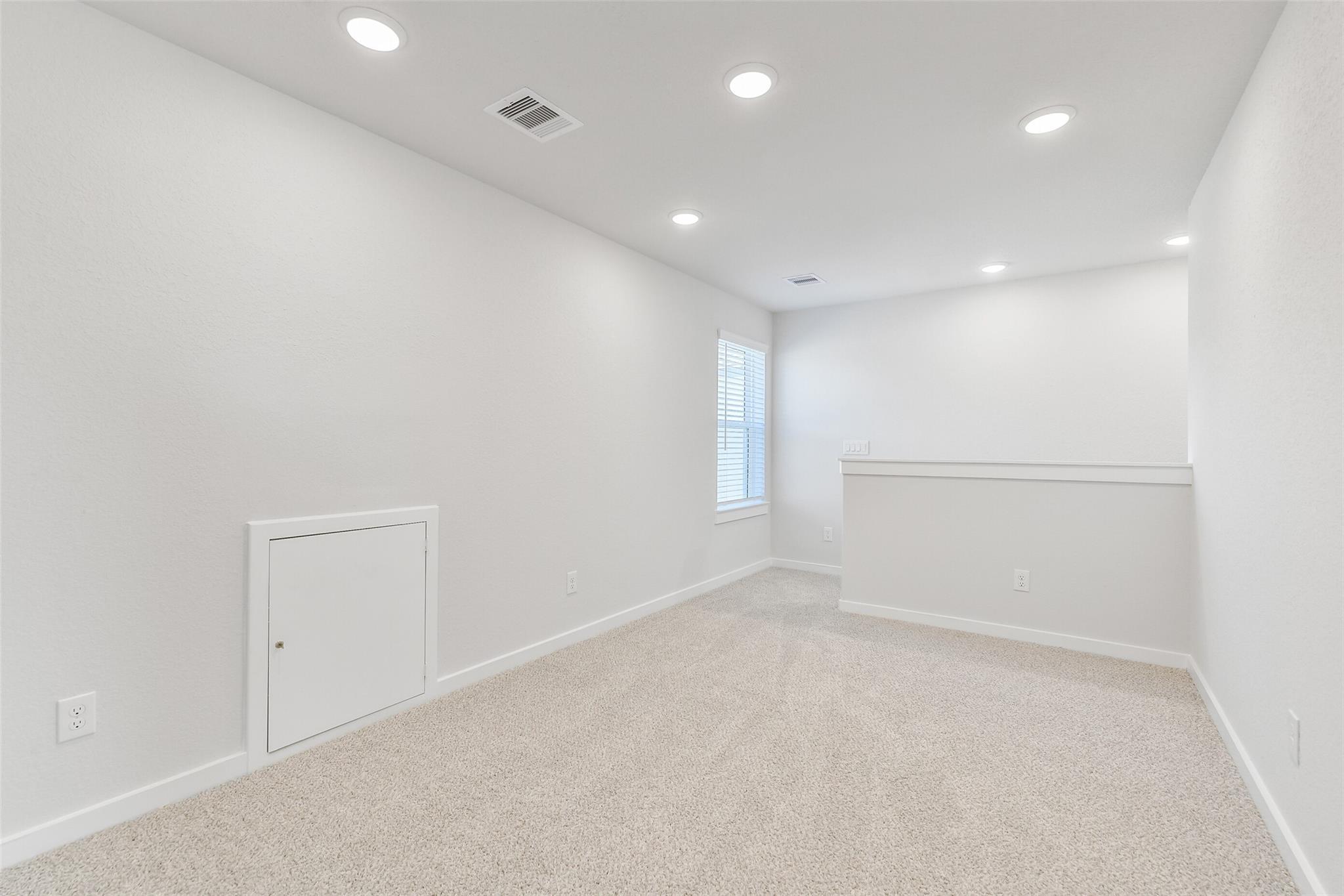 Bright upstairs loft with beige carpet, white walls, recessed lights, and window in Davidson Homes The Blanco E, Magnolia Texas