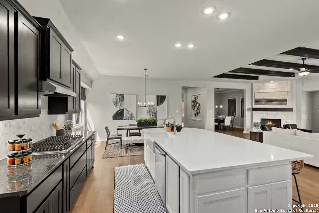 Modern open-concept kitchen with dark cabinets, white island, dining area, and cozy living room fireplace in Davidson Homes Summerlin B, Castroville, Texas
