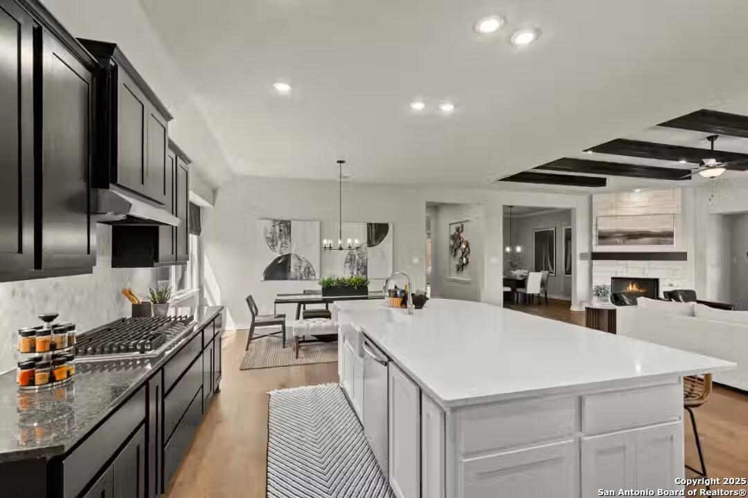 Modern open-concept kitchen with dark cabinets, white island, dining area, and cozy living room fireplace in Davidson Homes Summerlin B, Castroville, Texas
