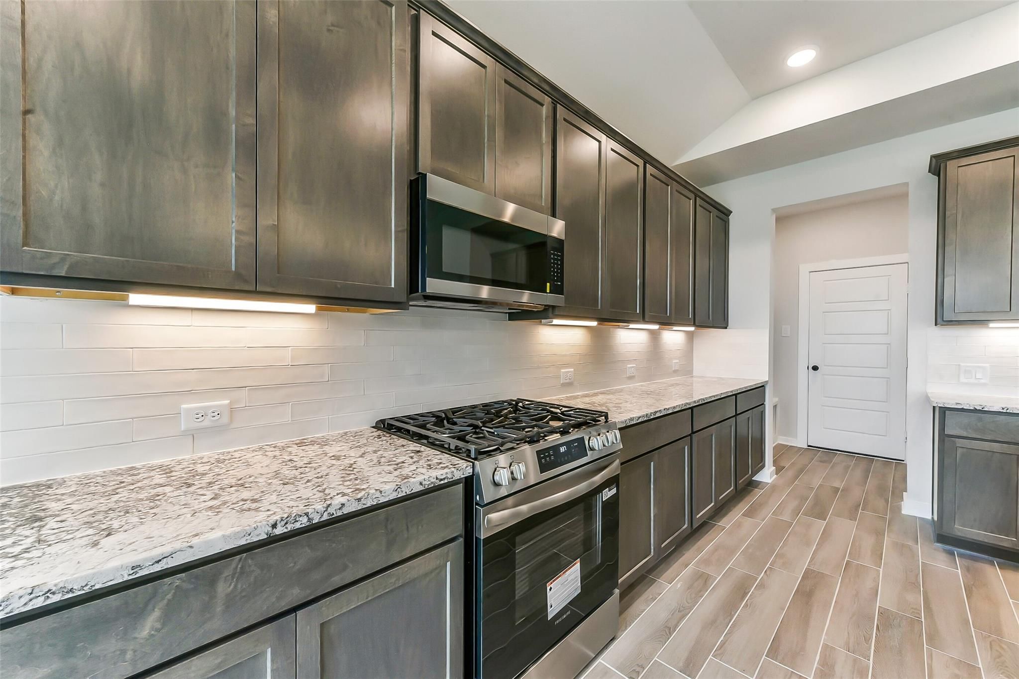 Modern kitchen with gray shaker cabinets, quartz counters, white subway backsplash, stainless gas range in Davidson Homes Sequoia C, Crosby TX