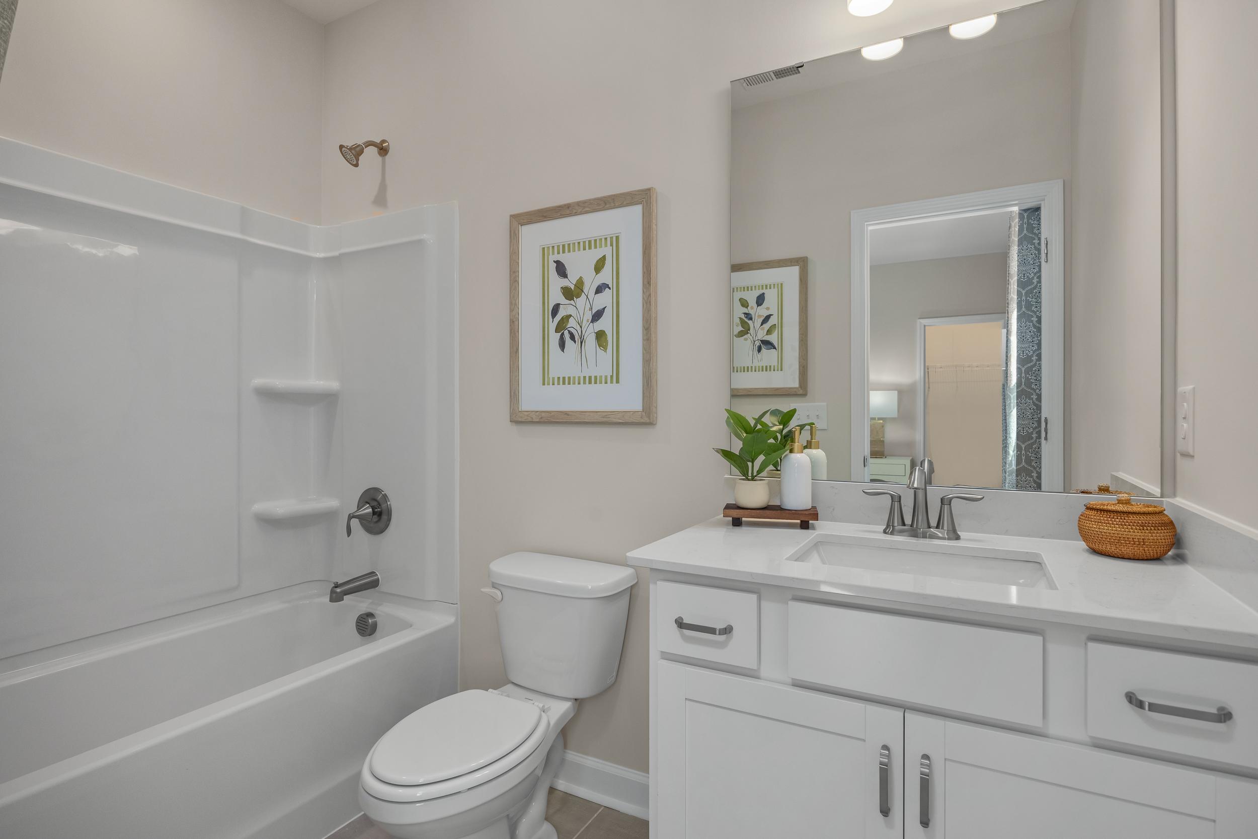 Spacious master bathroom in The Hickory II featuring white tub, double sink vanity, large mirror, and botanical accents