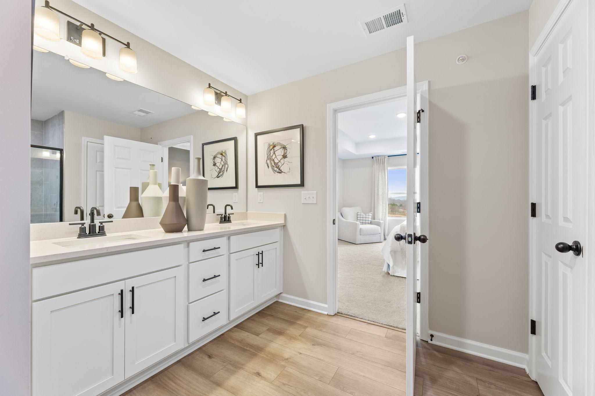 Elegant master bathroom double vanity with quartz countertop, white cabinets, and open bedroom door in Davidson Homes The Durham B, Cumming, GA