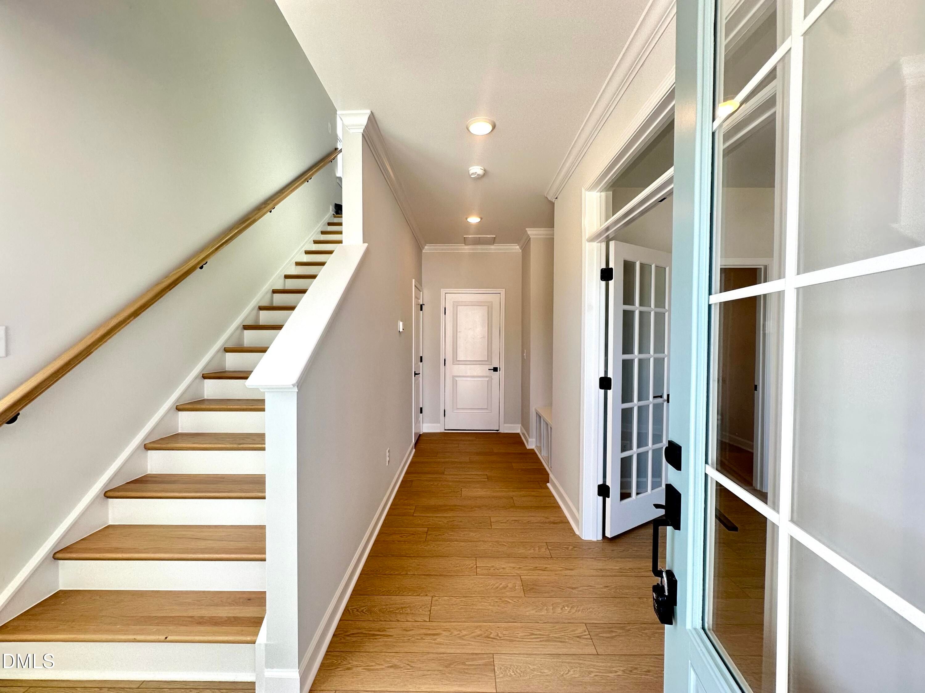 Elegant oak staircase with white risers and hallway featuring hardwood floors, French doors in Davidson Homes The Avery, Knightdale, NC