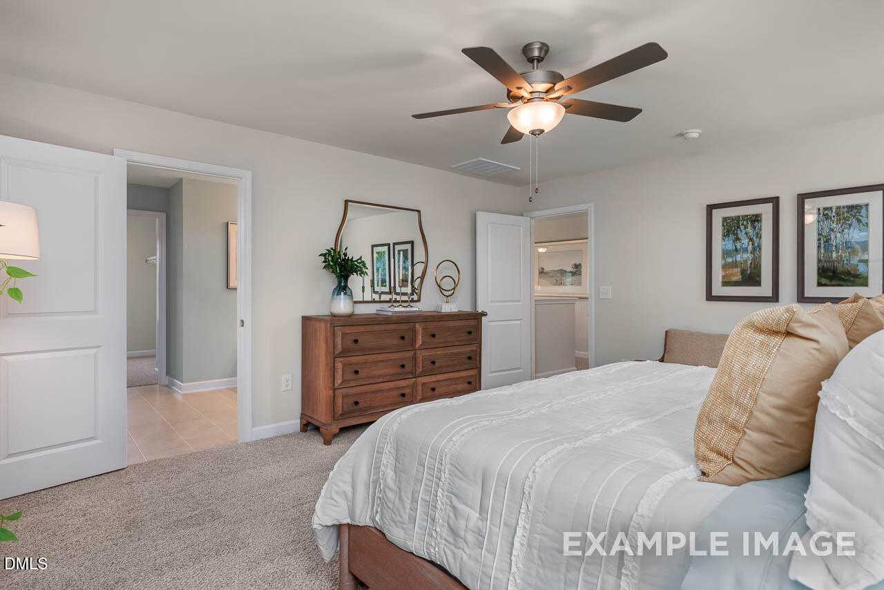 Spacious master bedroom with king bed, wooden dresser, ceiling fan, and tropical art in Davidson Homes The Willow B, Lillington, NC