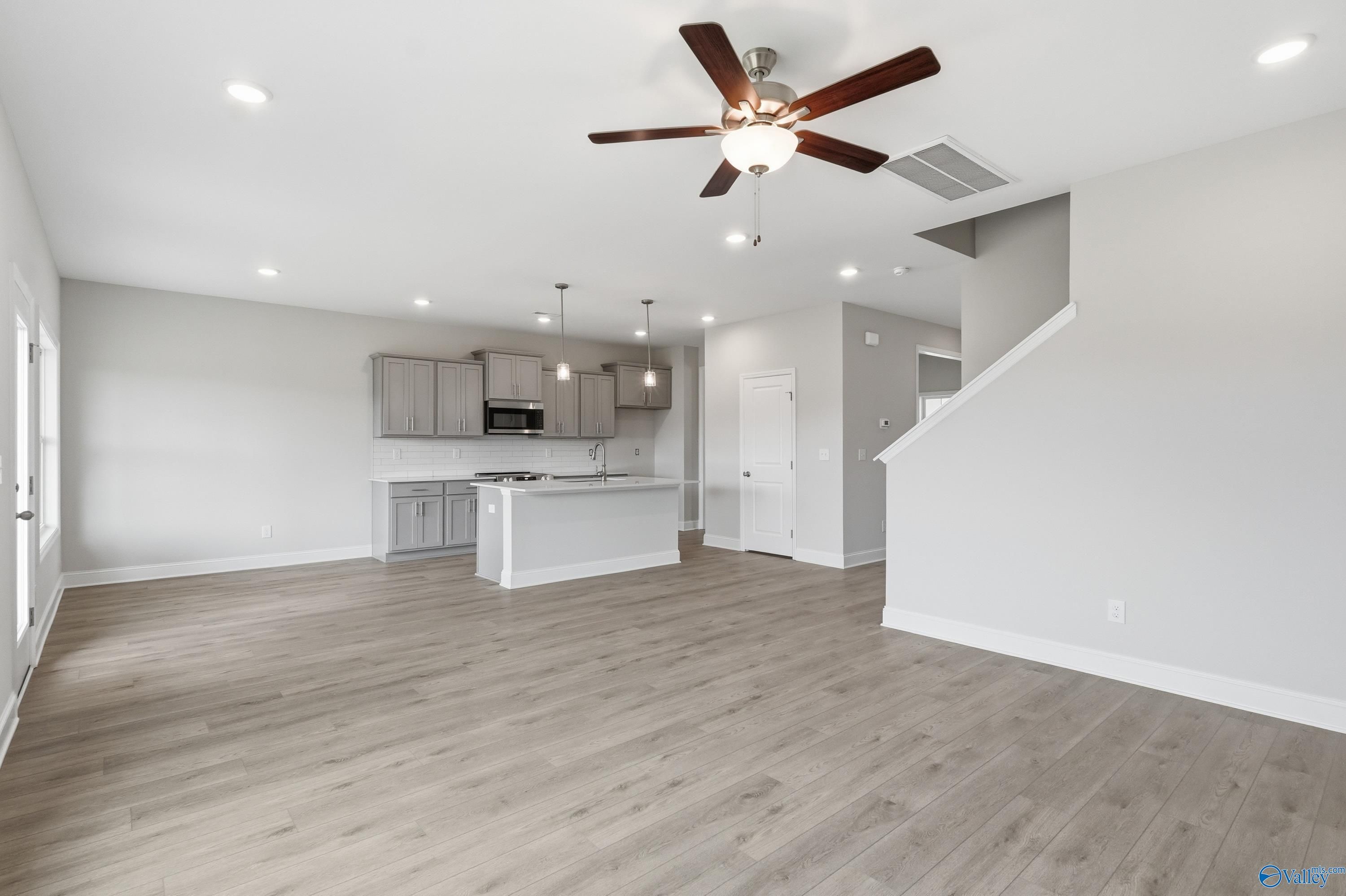 Open-concept living room and kitchen with hardwood floors, white island cabinets, ceiling fan in Davidson Homes The Shelby B, New Market, AL
