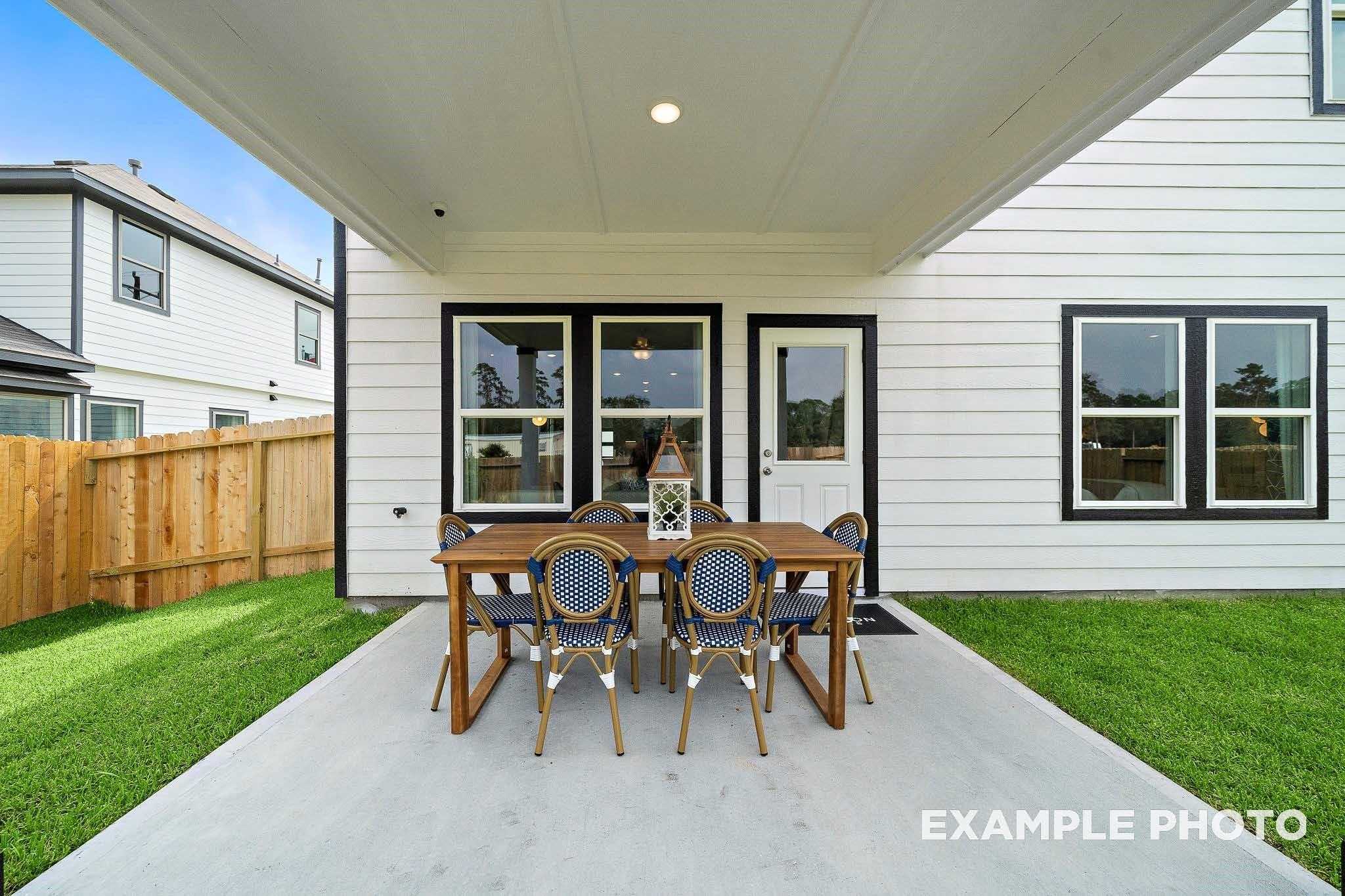Covered back patio with wooden dining table and blue chairs on concrete slab, lush green lawn in Davidson Homes San Marcos E, Conroe, TX