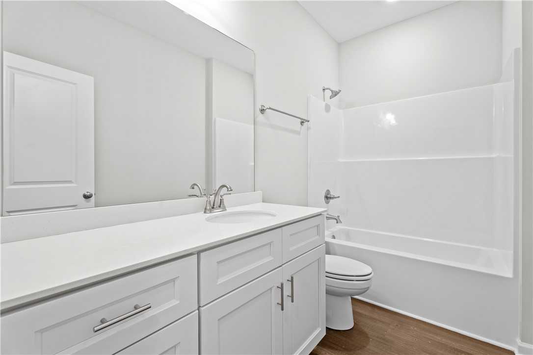 Modern white bathroom with quartz vanity, single sink, mirror, tub-shower combo, toilet in Evermore Homes The Orion, Cusseta AL