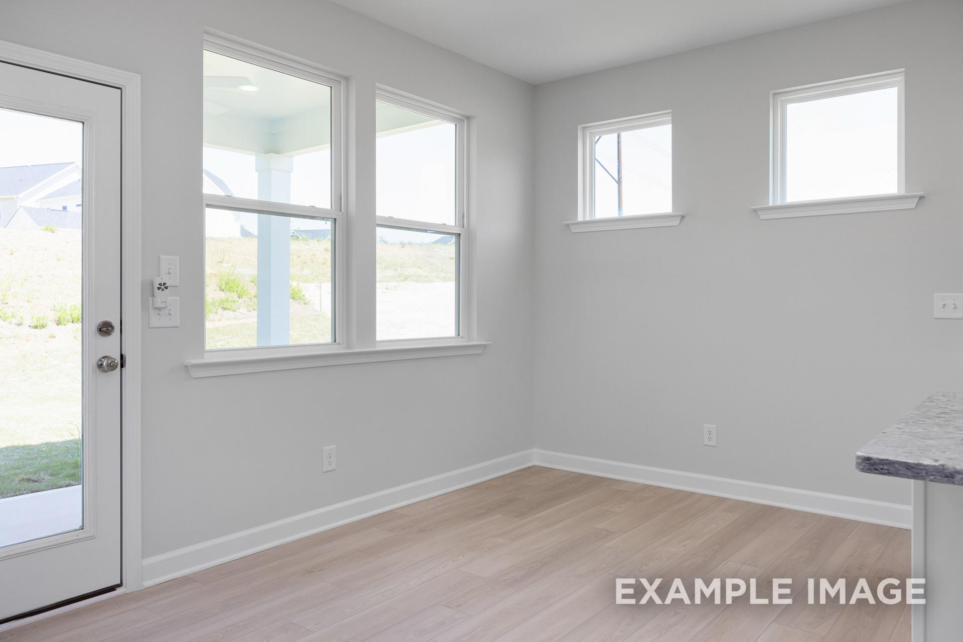 Spacious living room in The Gavin B with large windows, gray walls, light wood floors, and kitchen nook overlooking yard