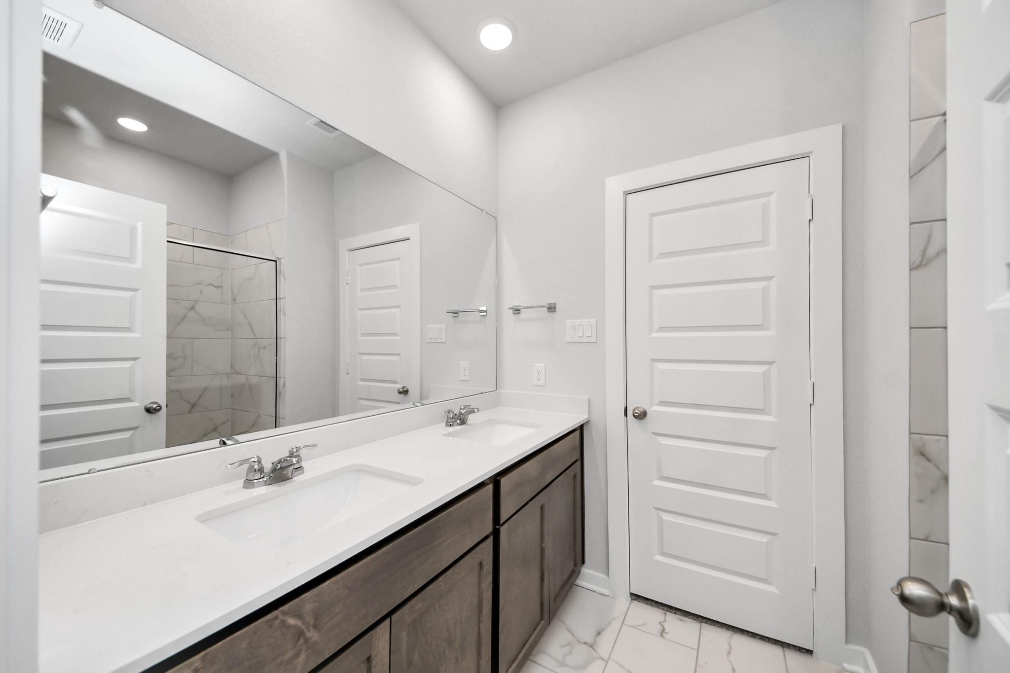 Modern bathroom with dual vanity and marble-look tile in The Sabine E floor plan at Liberty Estates, Cleveland, Texas.