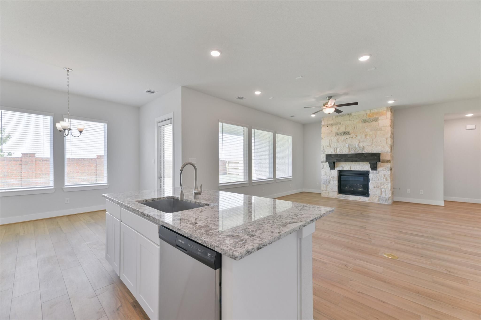 Open-concept kitchen with granite island, stainless dishwasher, and adjacent living room featuring stone fireplace in Davidson Homes The Edward A, Texas City