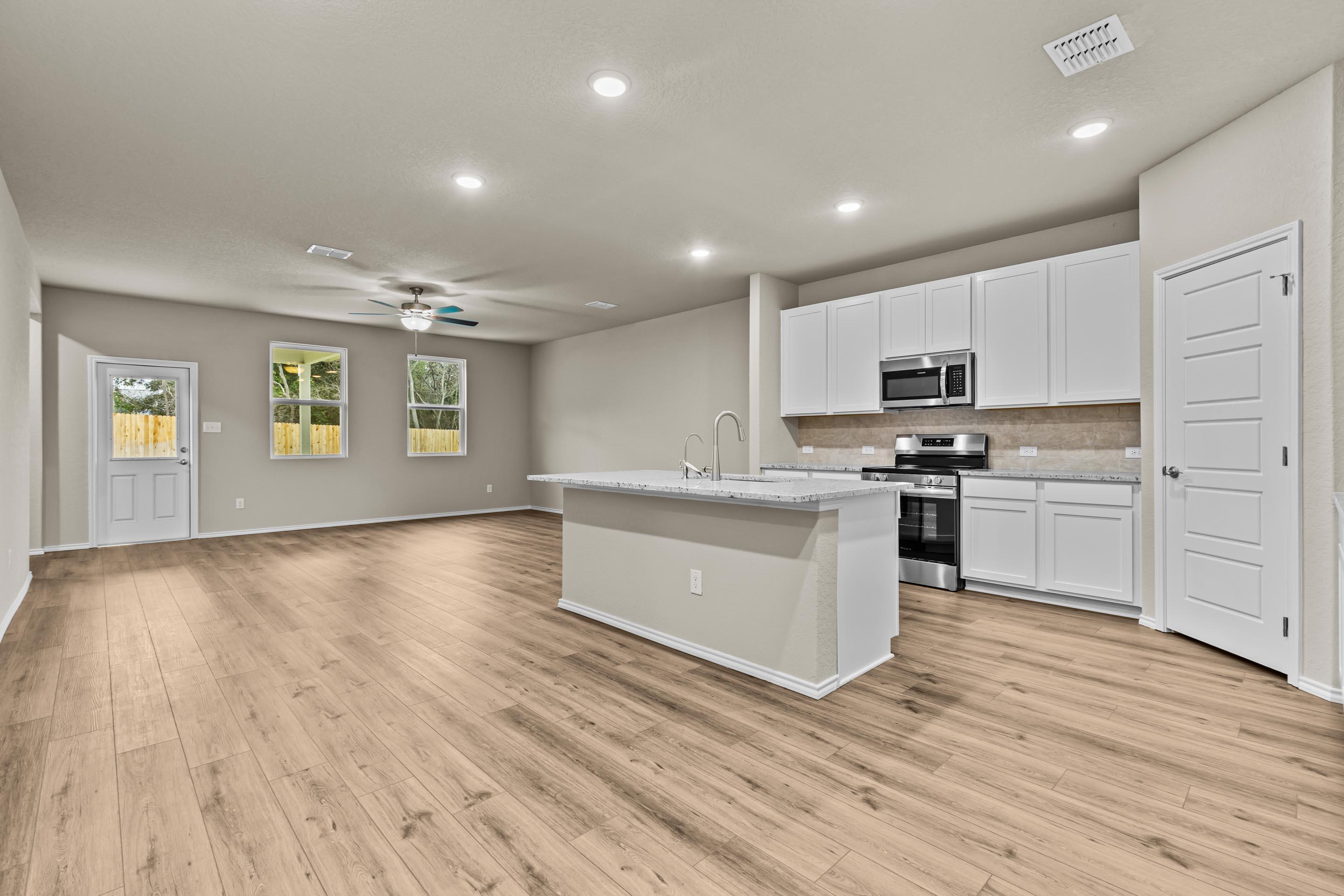 Modern open-concept kitchen with white cabinets, stainless appliances, granite island, and hardwood floors in Davidson Homes The Douglas F, San Antonio