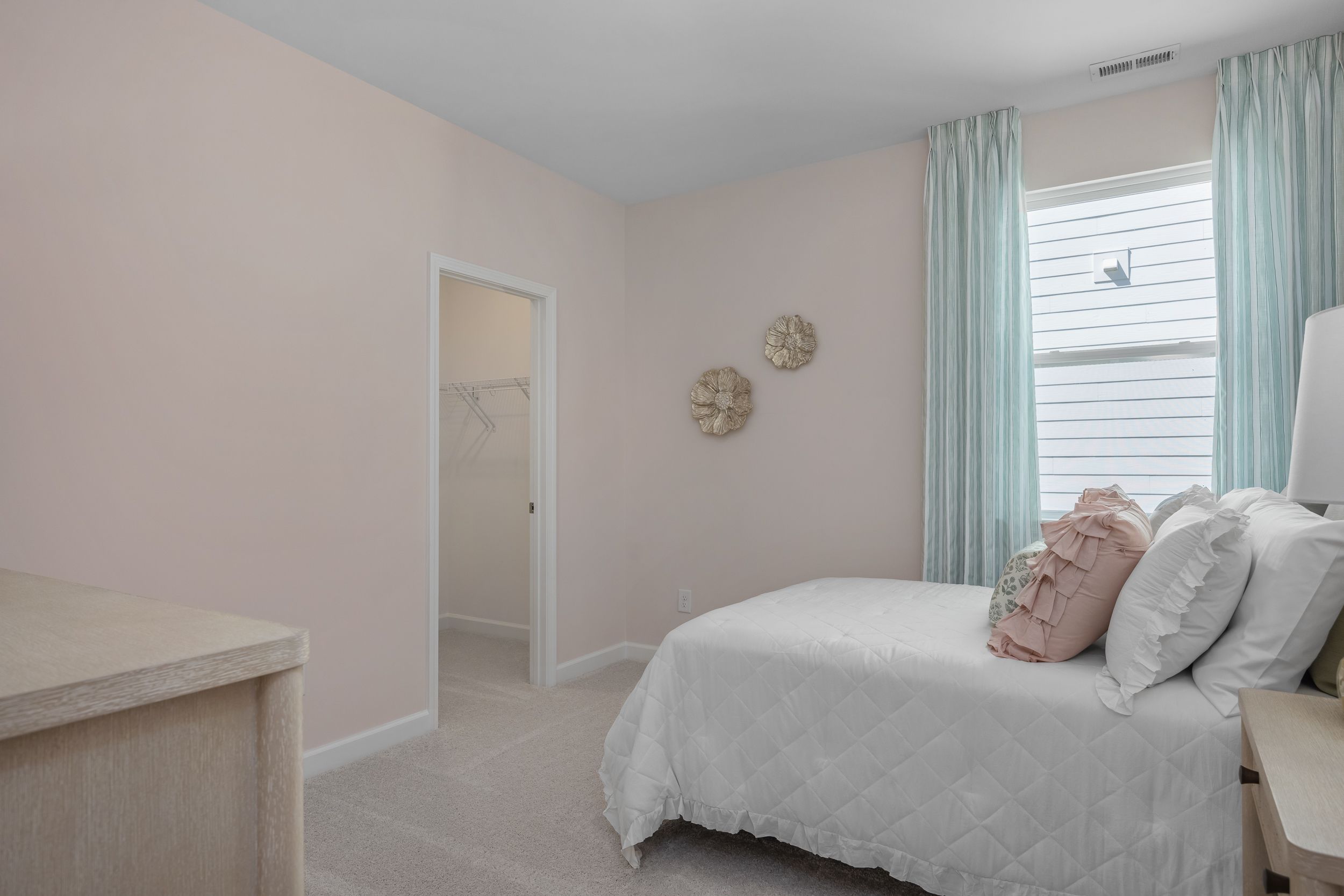 Cozy upstairs bedroom in The Hickory II A with pink walls, white bed, pink pillows, teal curtains, and wall decor