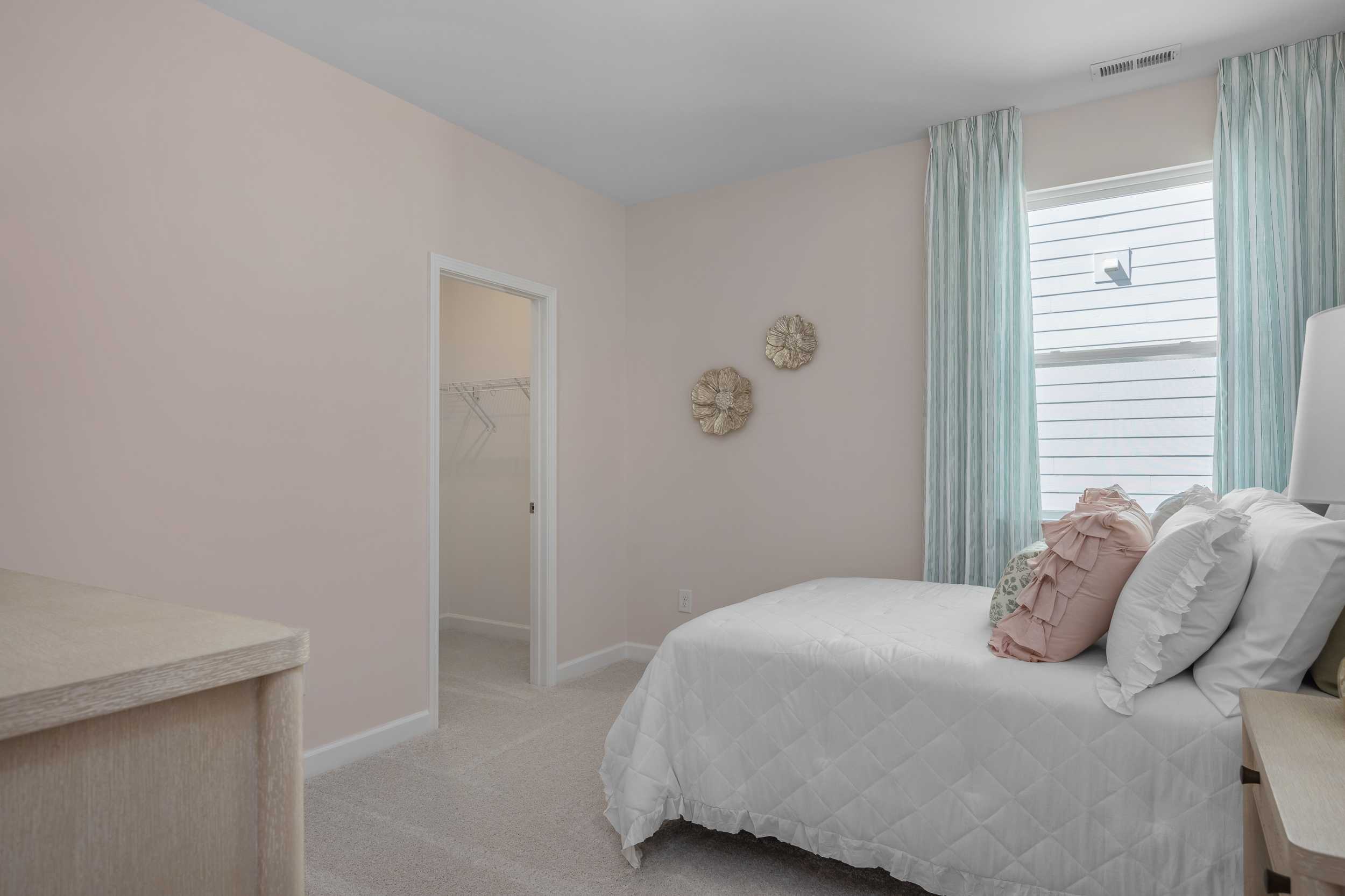 Cozy pink bedroom in The Hickory II E featuring white bed with ruffled pillows, shell decor, and teal curtains