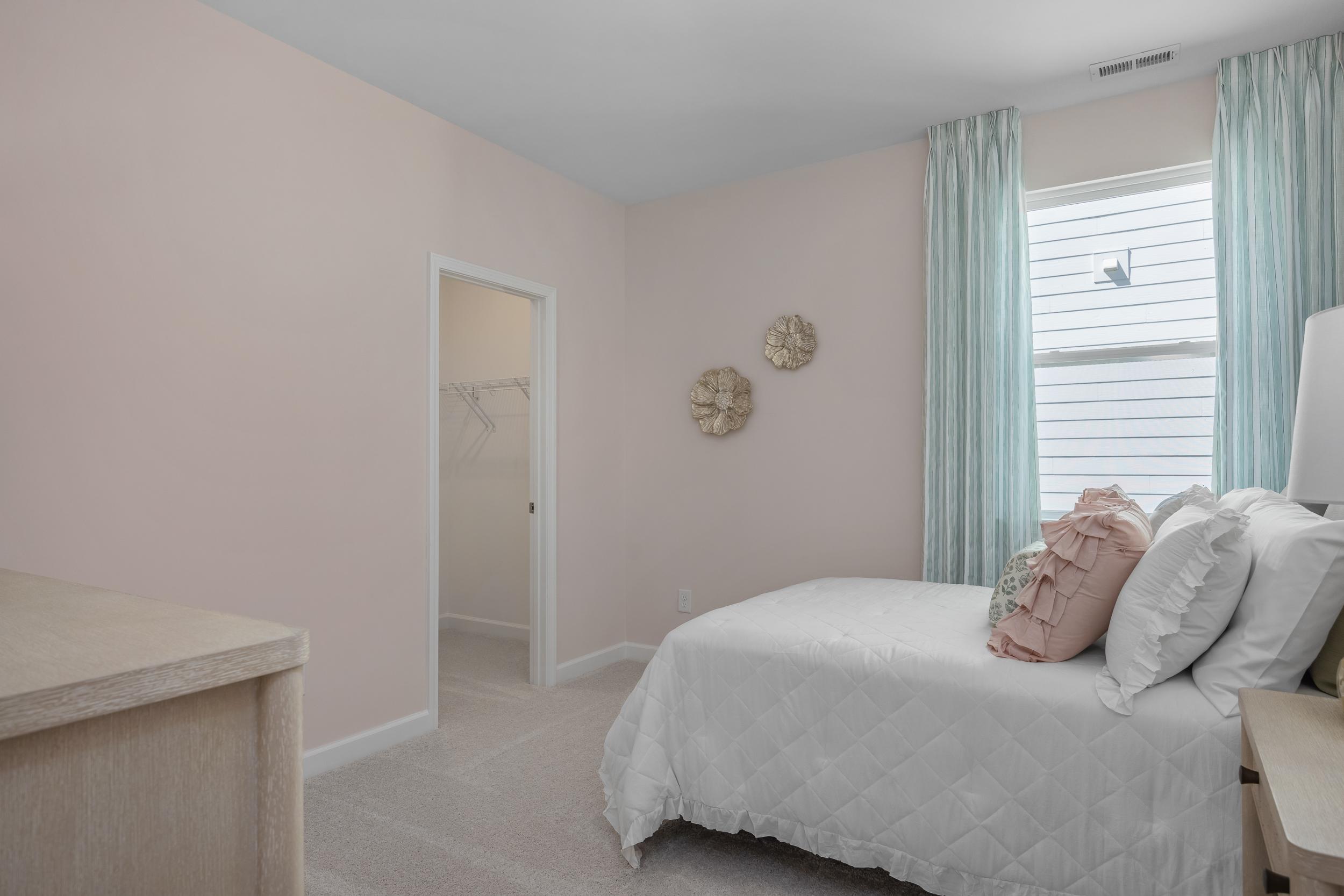 Serene pink bedroom in The Hickory II master suite by Davidson Homes, white bed with ruffled pillows, blue curtains, walk-in closet