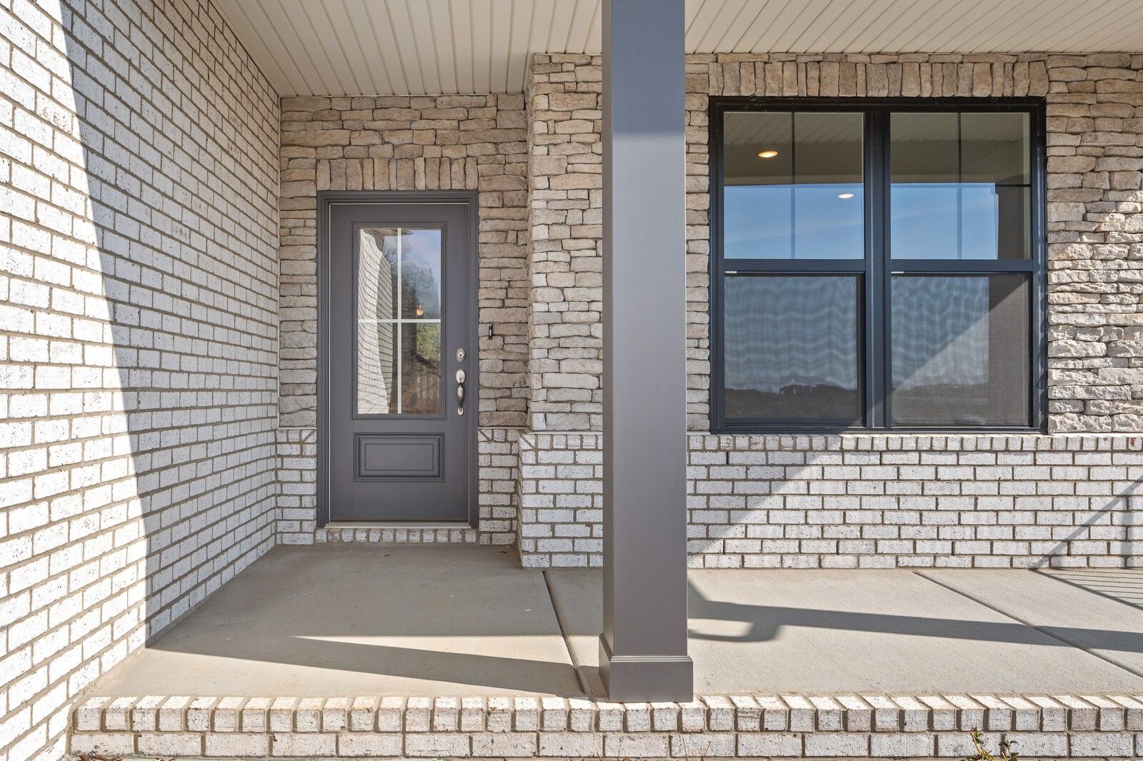 White brick two-story home exterior with gray glass door, large black-framed windows, and covered entry porch in Mt. Juliet, Tennessee