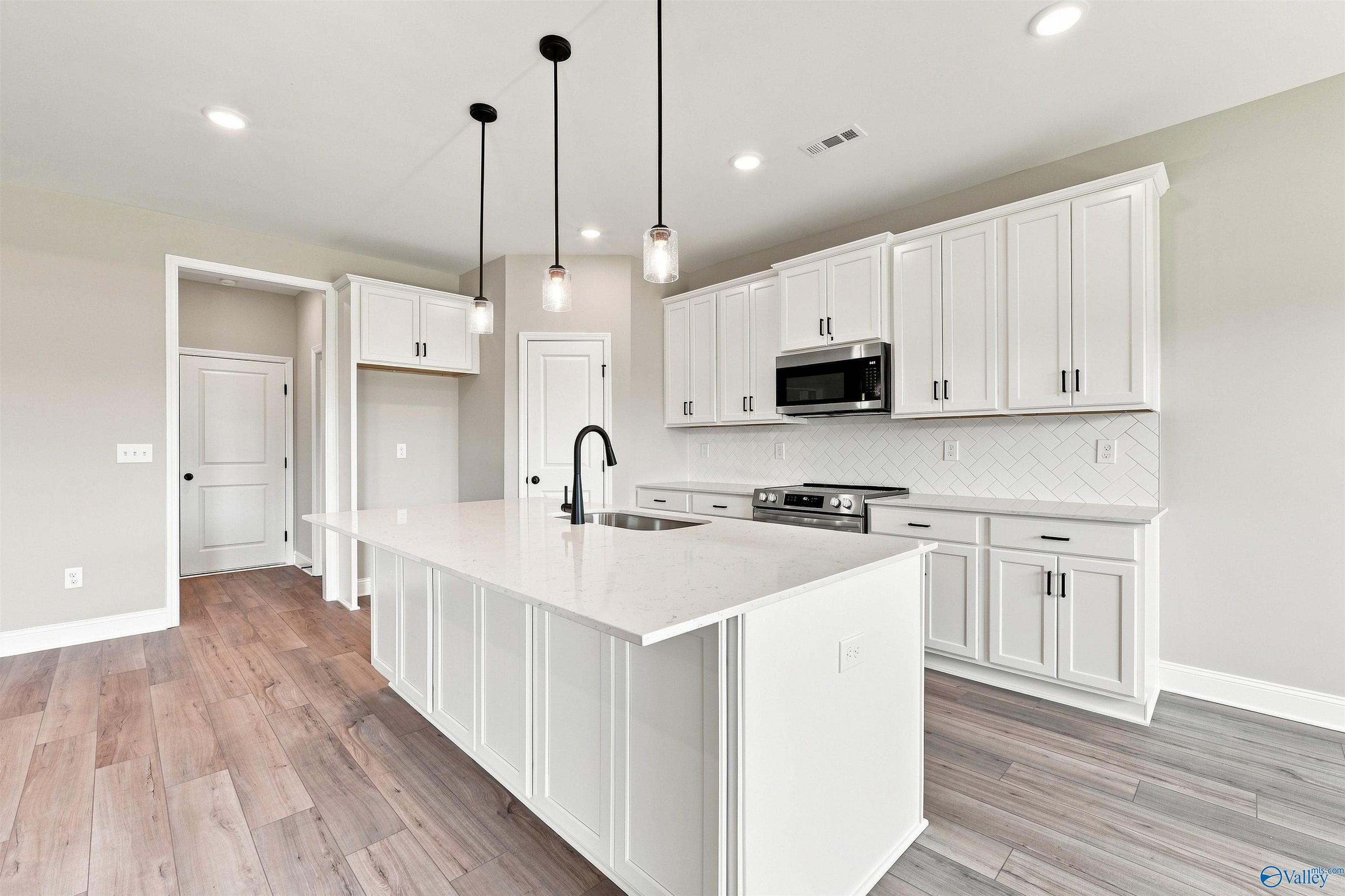 Modern kitchen with white cabinets, quartz island, and pendant lighting in The Montgomery floor plan, Kendall Downs, Toney.