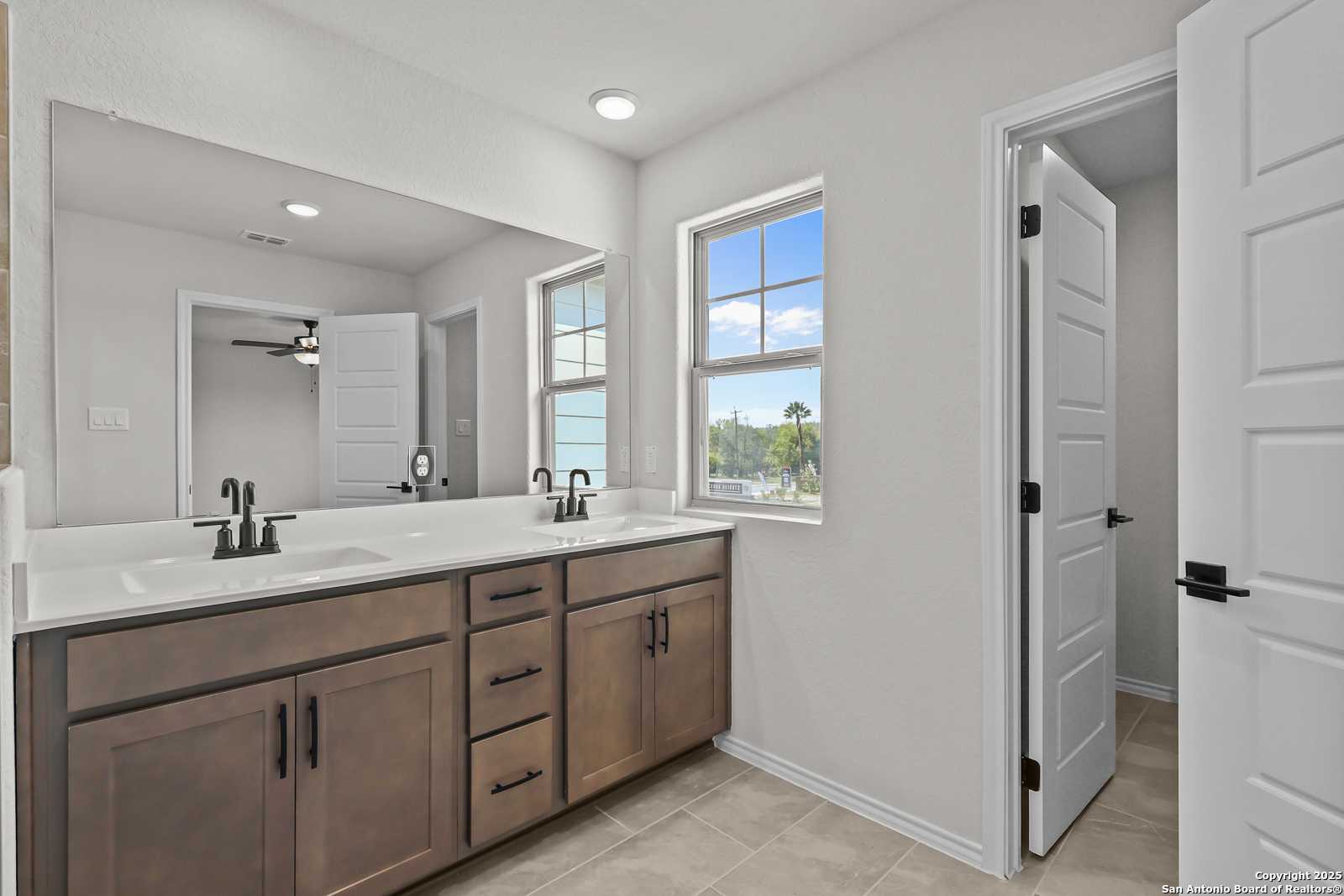 Elegant master bathroom with double vanity, large mirror, ceiling fan, and window view in Davidson Homes The Florence C, San Antonio