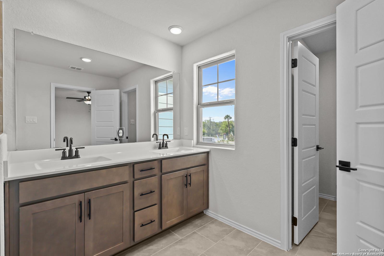 Elegant master bathroom with double vanity, large mirror, ceiling fan, and window view in Davidson Homes The Florence C, San Antonio