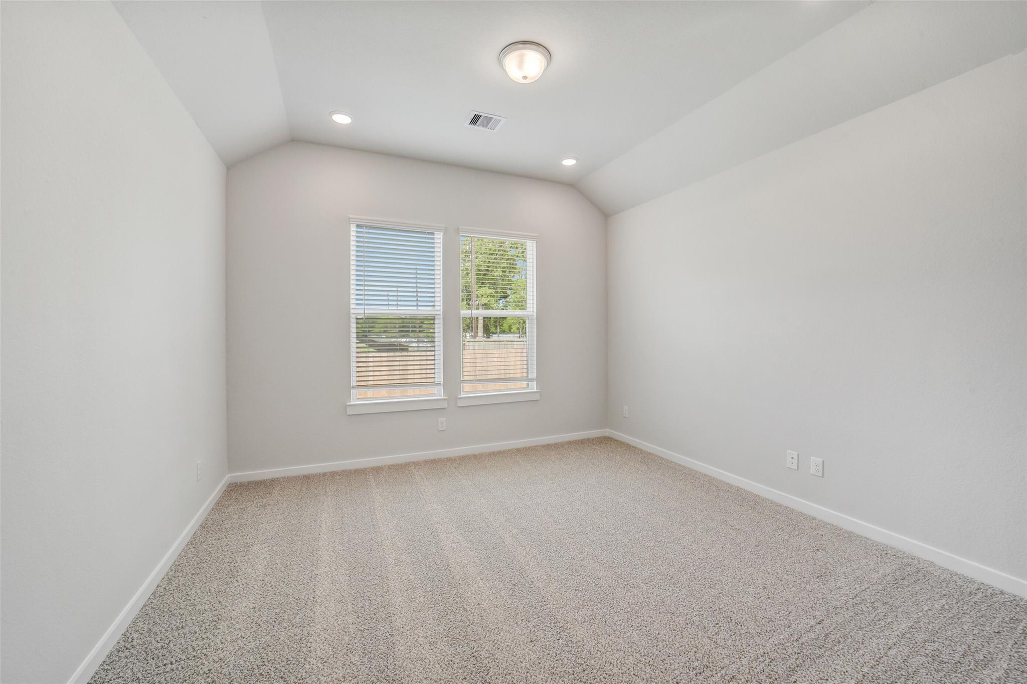 Bright secondary bedroom with vaulted ceiling, dual windows, blinds, and plush carpet in Davidson Homes The Acadia C, Magnolia, Texas
