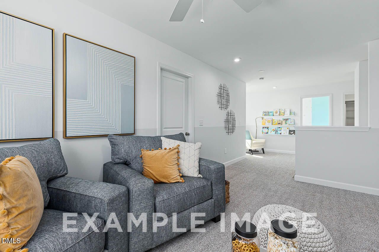 Bright upstairs loft with gray armchairs, ceiling fan, and carpet in Davidson Homes The Ash C, Lillington, NC