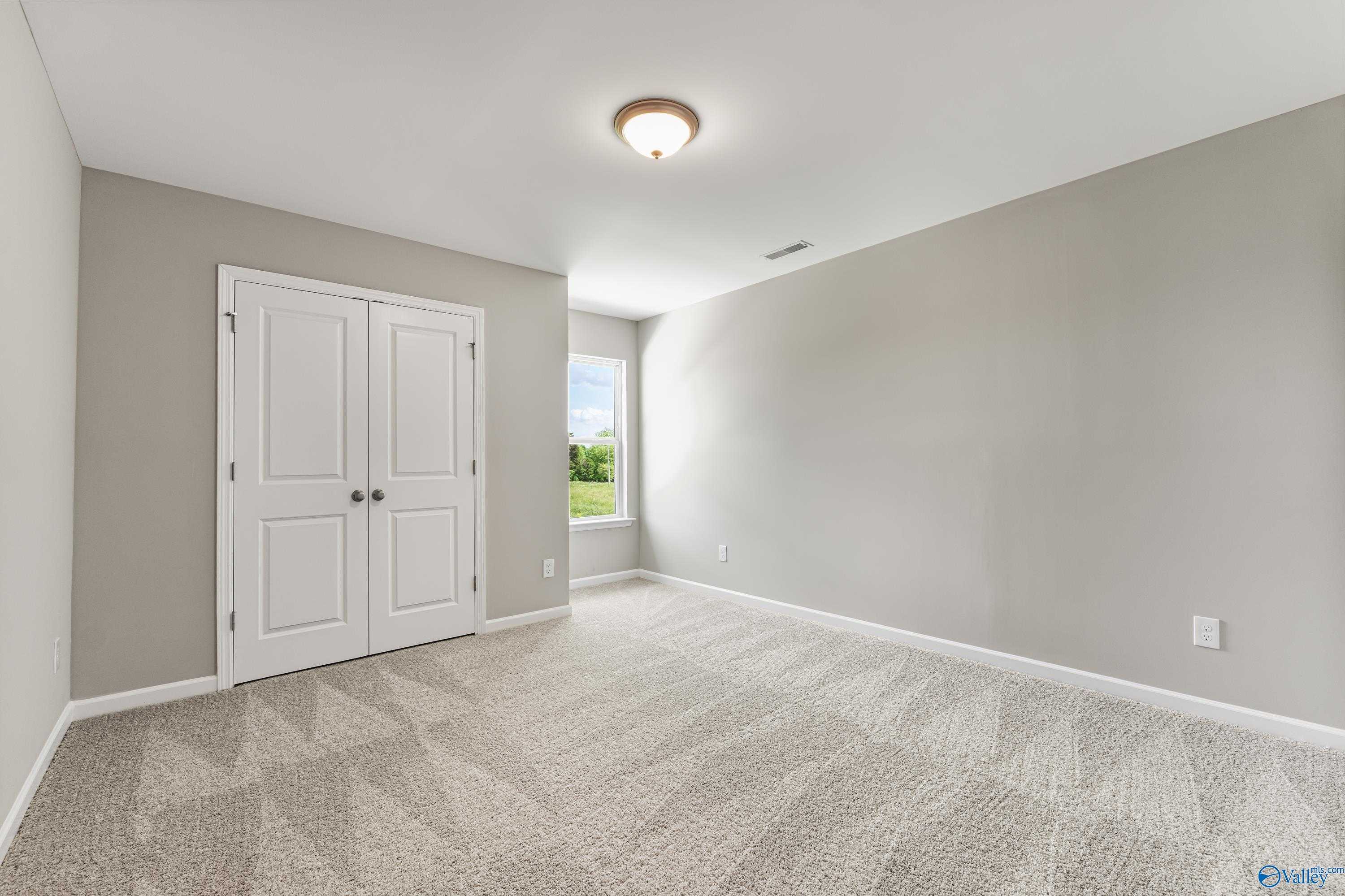 Spacious bedroom with light gray walls, white double closet doors, beige carpet, and window view in Davidson Homes The Haven, Huntsville, Alabama