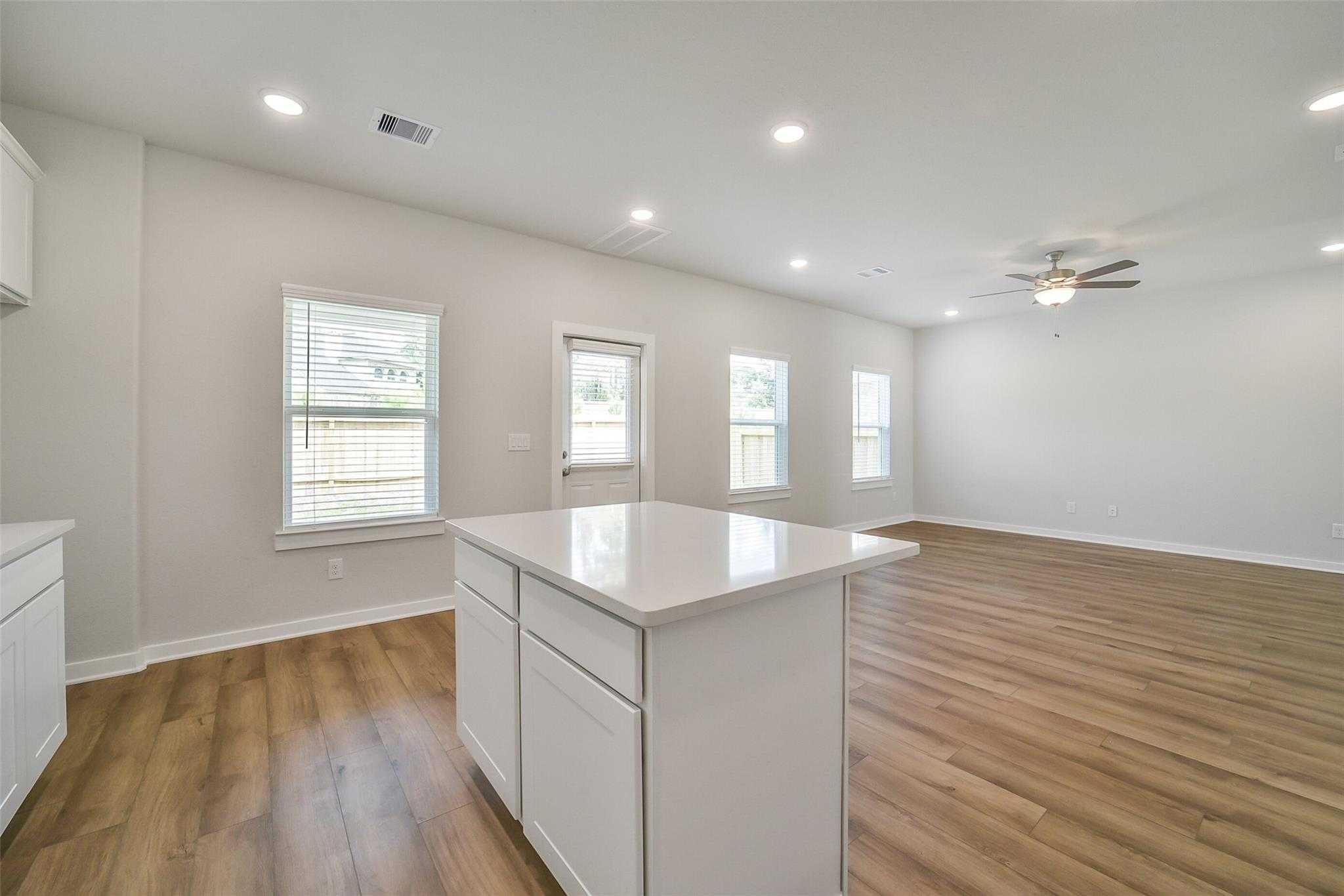 Bright open kitchen with white island, hardwood floors, large windows, and patio door in Davidson Homes Trinity F, Magnolia Texas