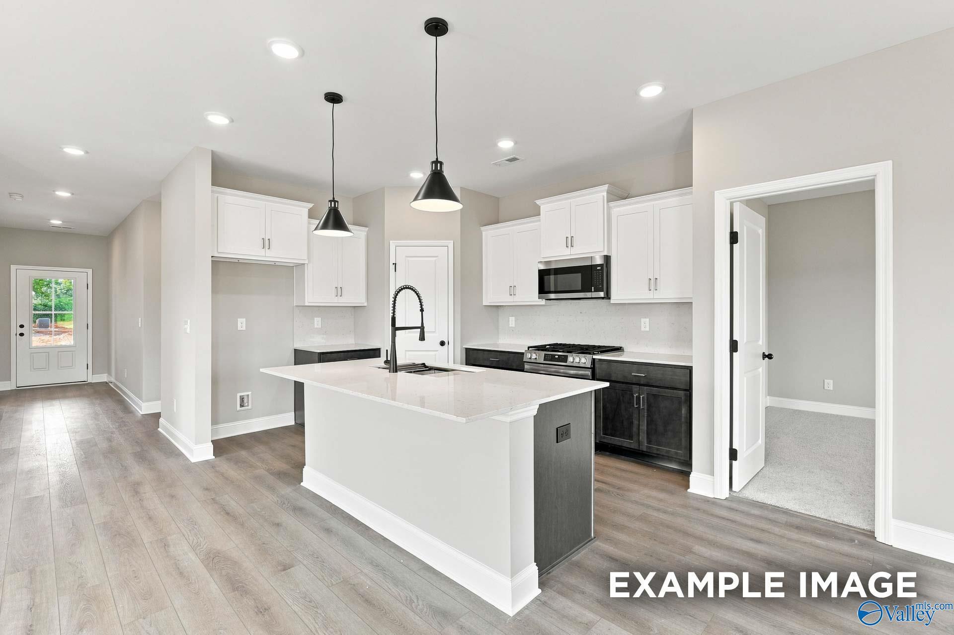 Modern kitchen with white cabinetry, dark island, and pendant lights in The Franklin D floor plan at Forest Glen, Hazel Green, Alabama