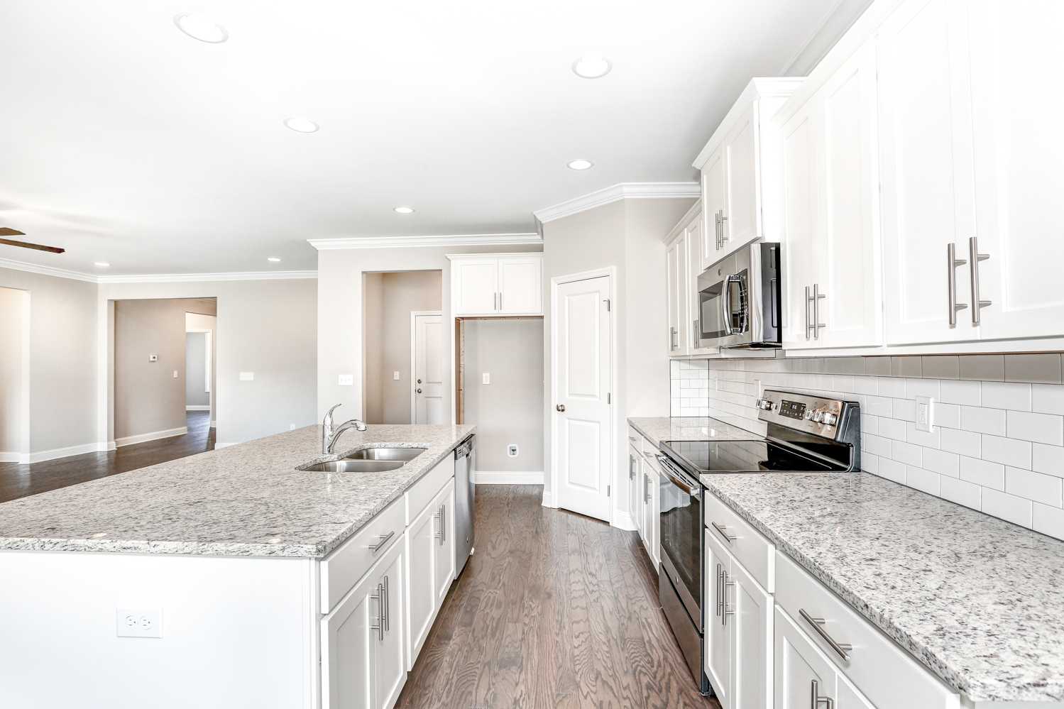 Spacious open kitchen in The Montgomery home featuring white shaker cabinets, granite island with sink, stainless steel appliances, subway tile backsplash