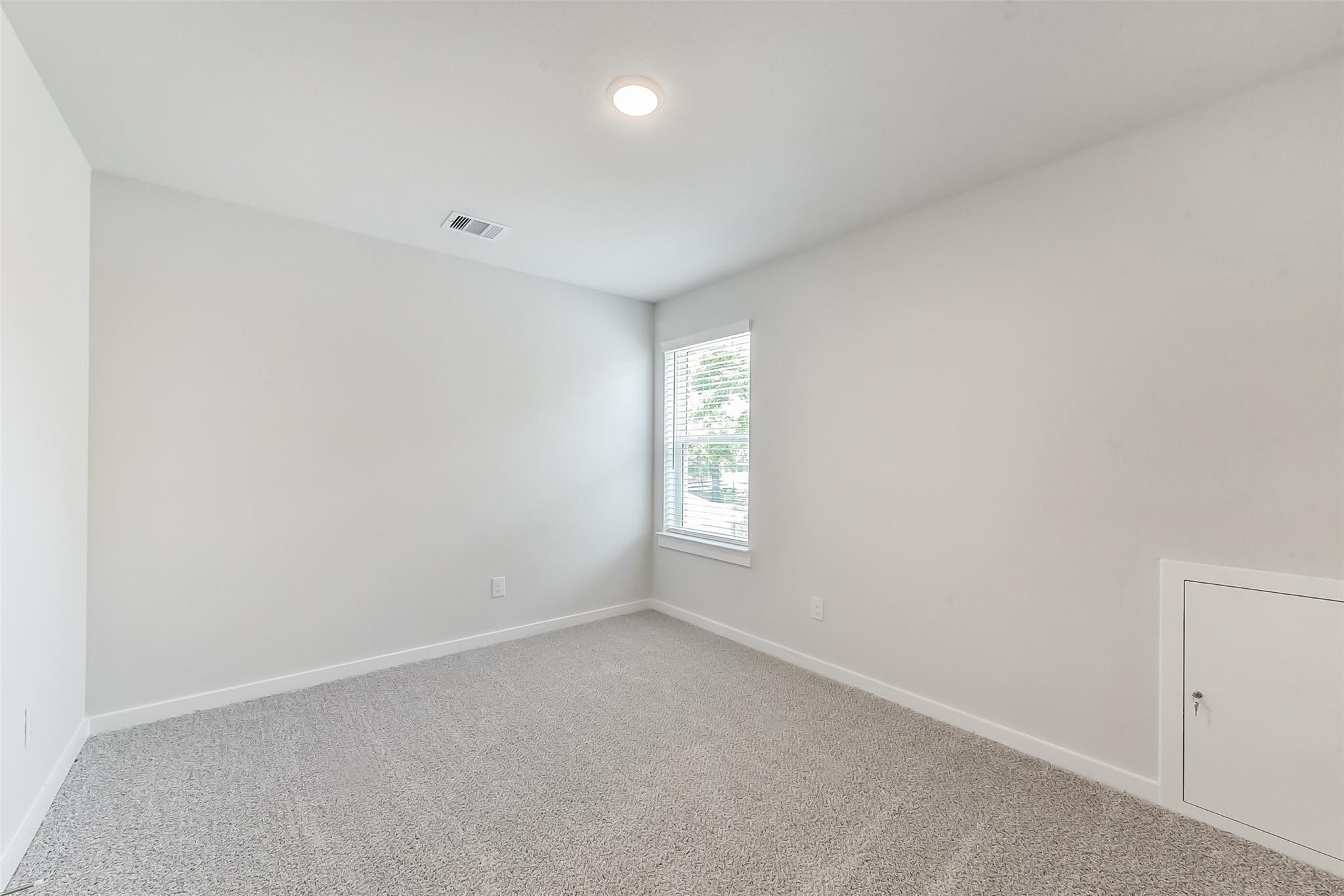 Empty bedroom with light gray walls, carpet floor, large window, and outlets in Davidson Homes The Brazos E, Magnolia, Texas