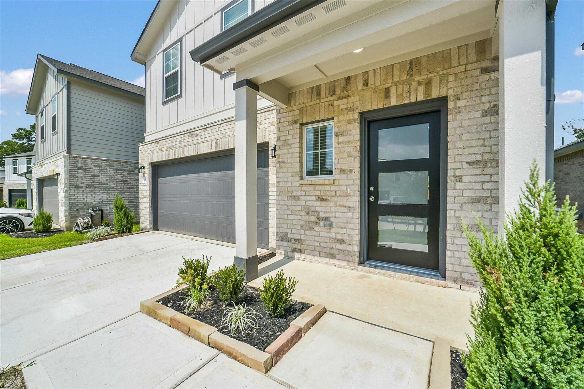 Modern two-story brick home with covered front porch, two-car garage, and landscaped driveway in Lakes at Black Oak, Magnolia, Texas